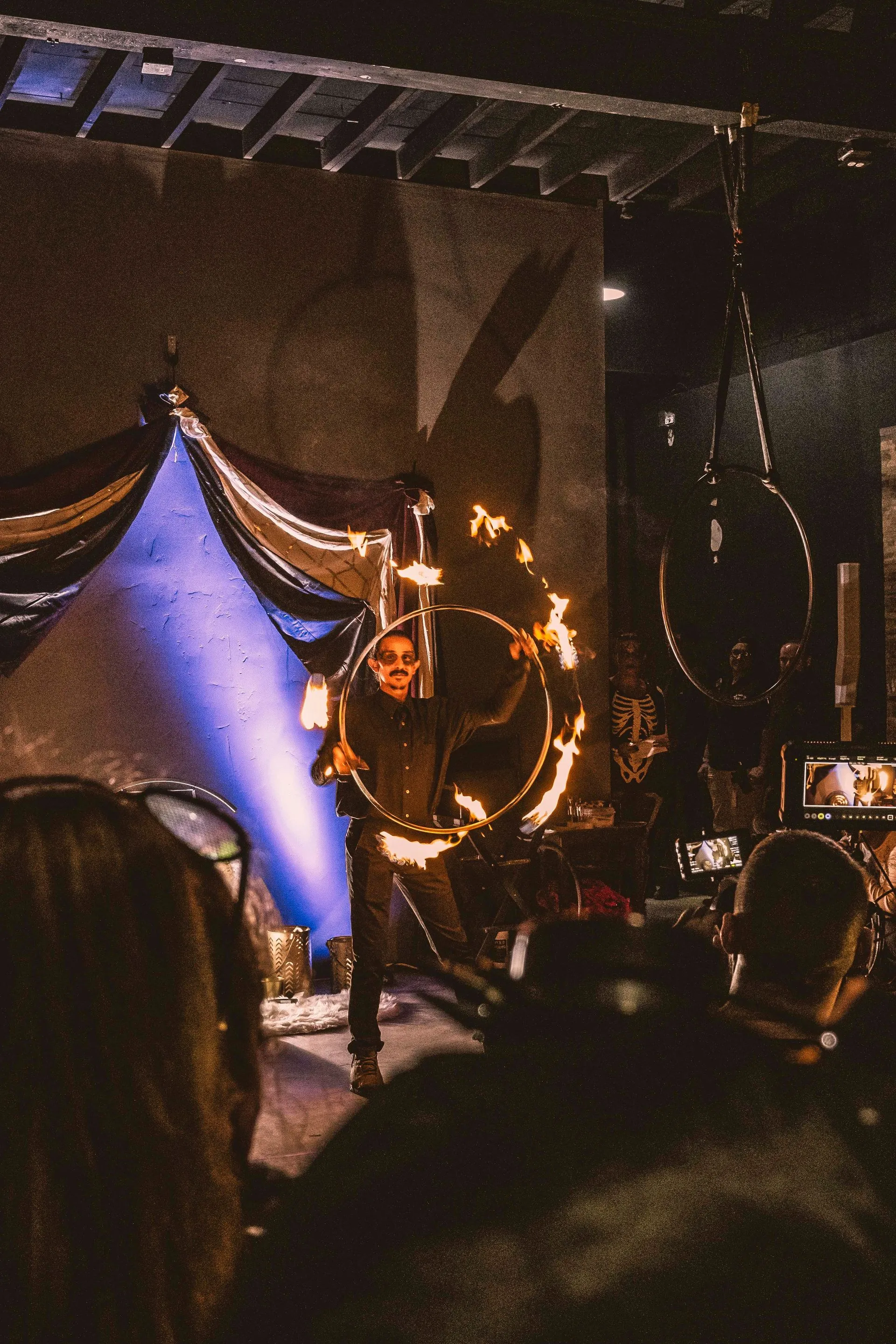 A man is standing on a stage holding a fire hoop in front of a crowd.