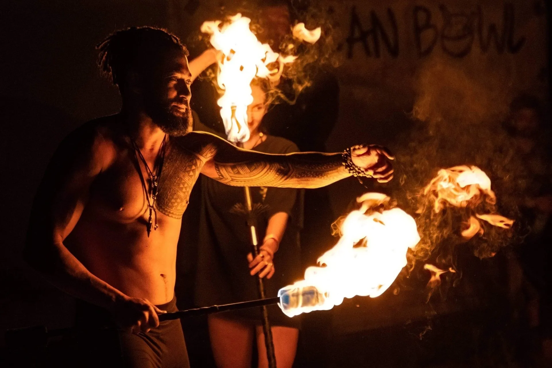 A shirtless man is holding a stick with flames coming out of it.