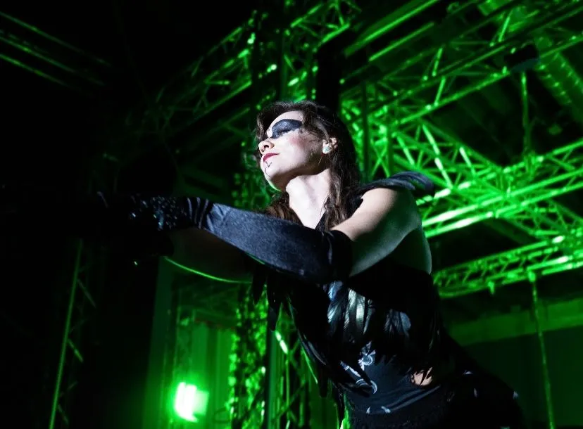 A woman in a black dress is dancing in front of a green light.