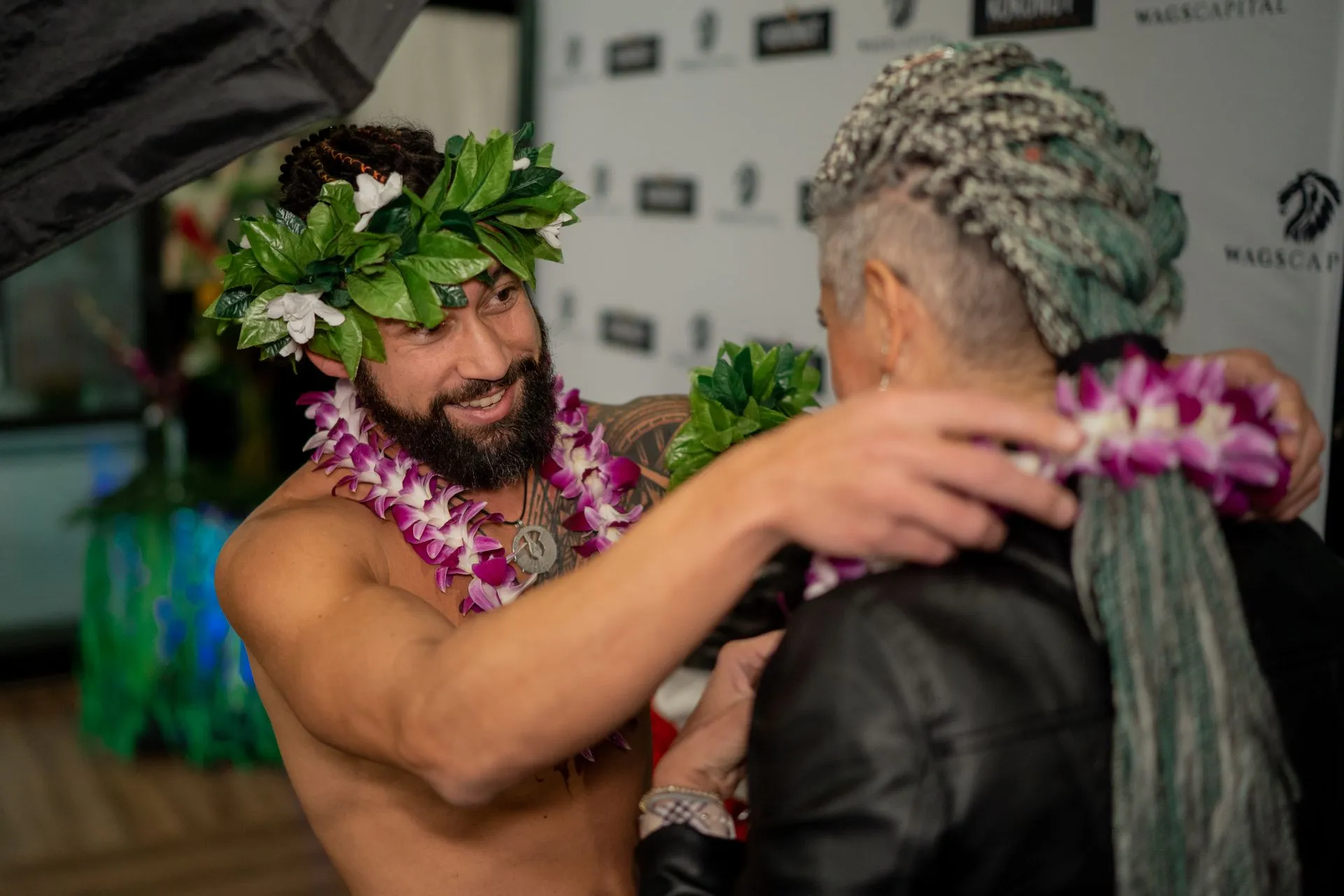 A shirtless man wearing a lei is hugging a woman.
