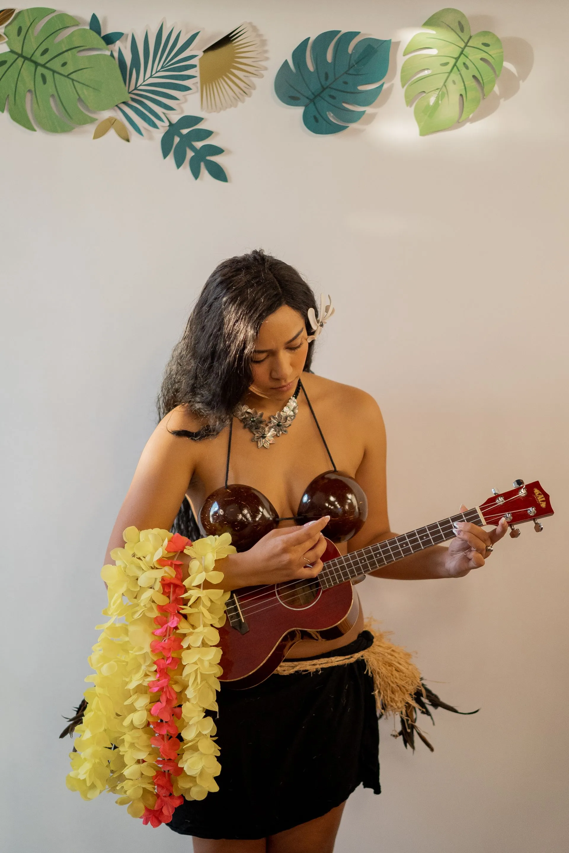 A woman in a coconut bra is playing a ukulele.