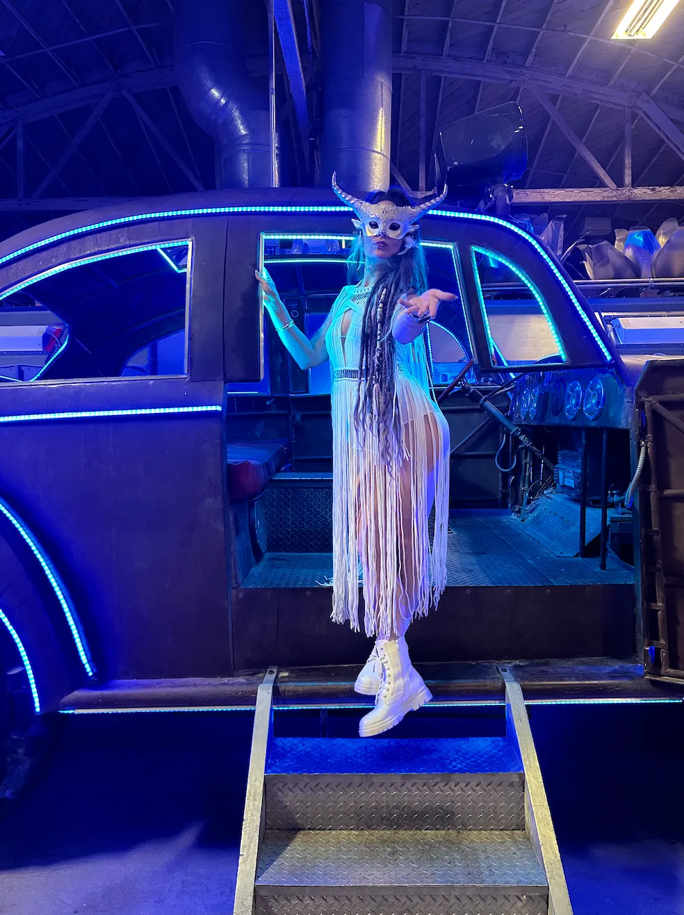 A woman in a mask is standing in front of a car.