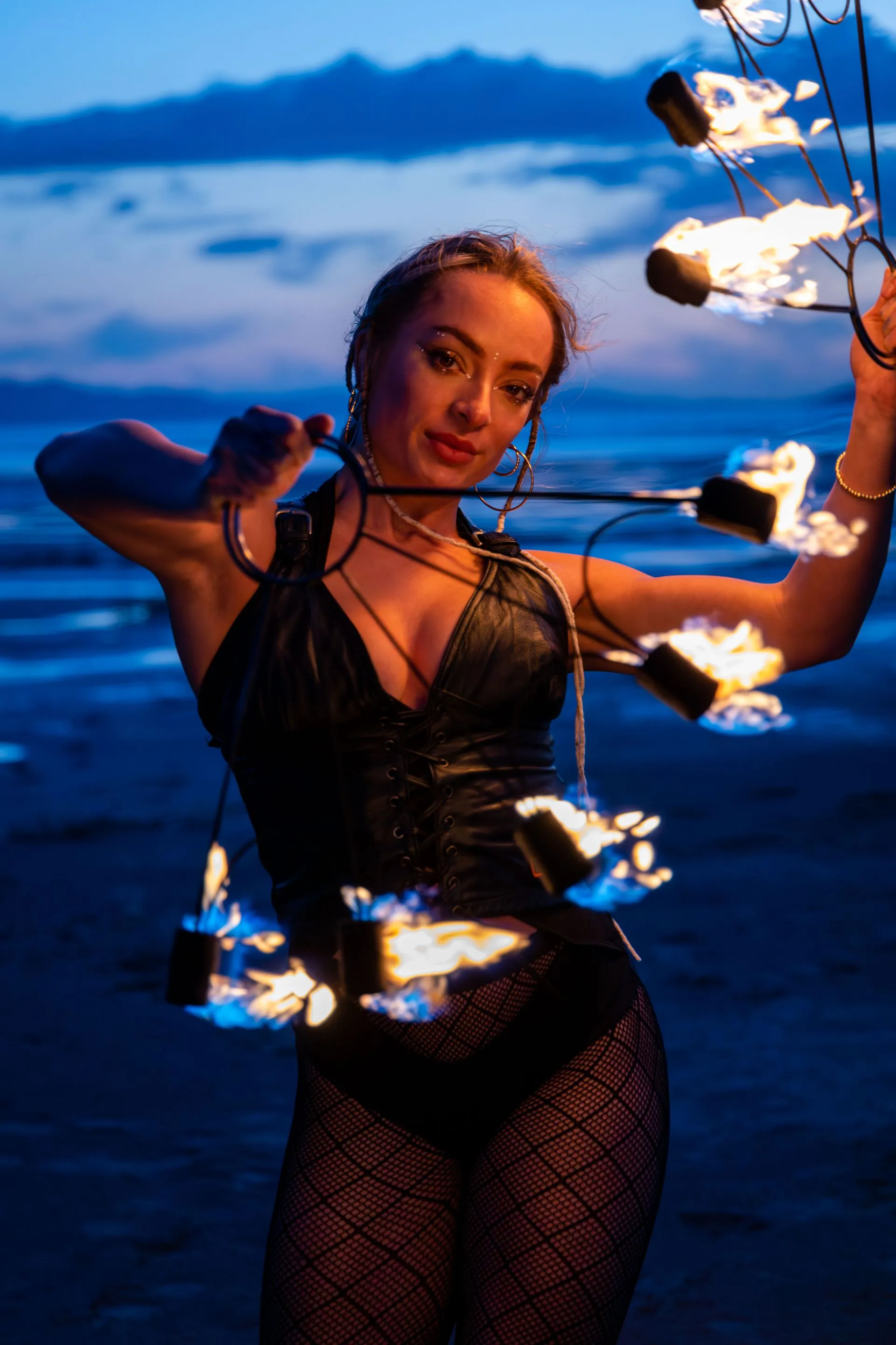 A woman is holding a bunch of fire sticks on a beach.