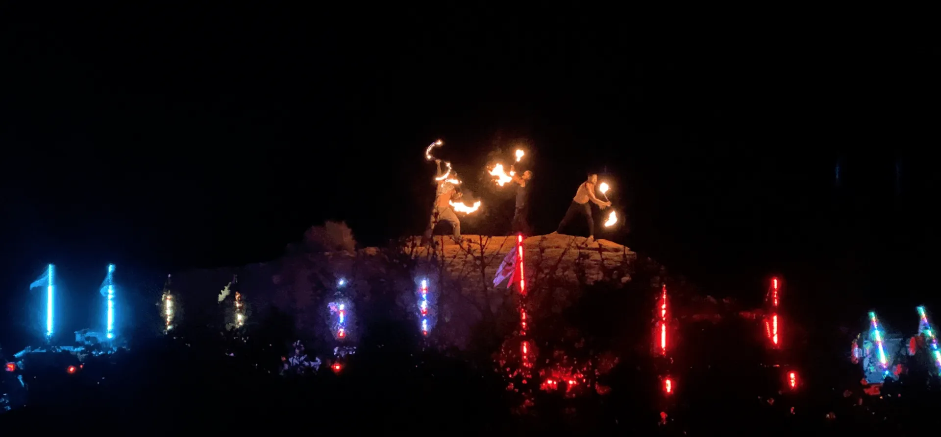 A group of people are standing on top of a hill holding fire.