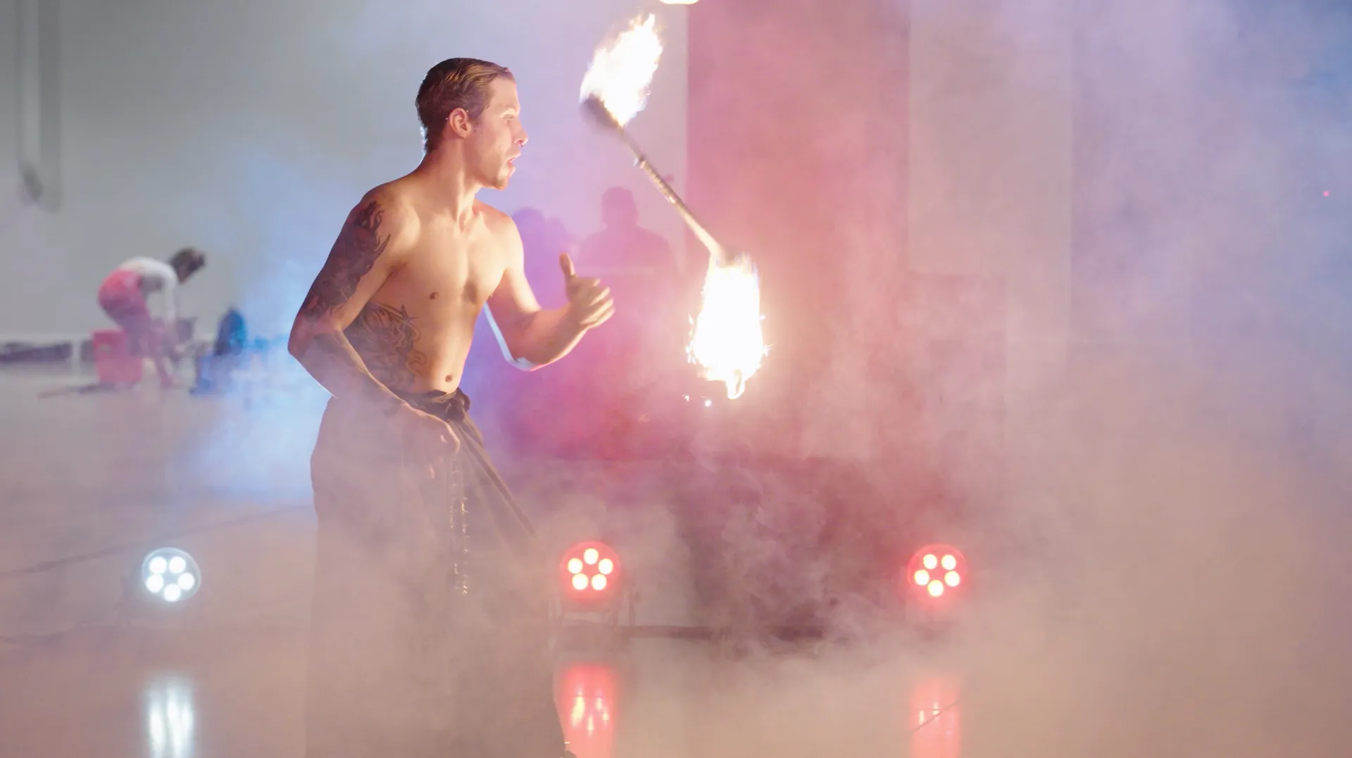 A shirtless man is holding a fire torch in a dark room.