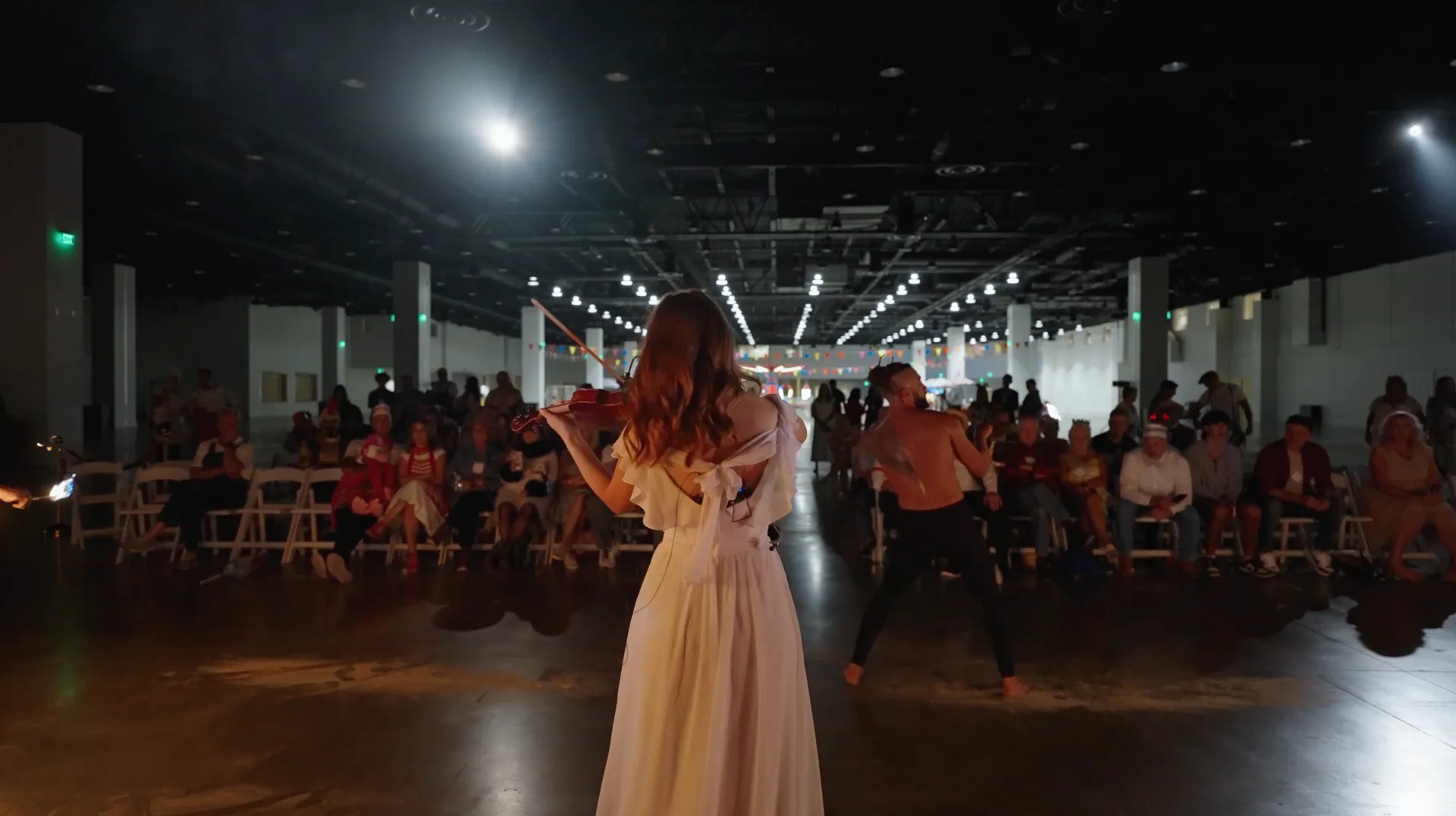 A woman in a white dress is standing in front of a crowd of people.