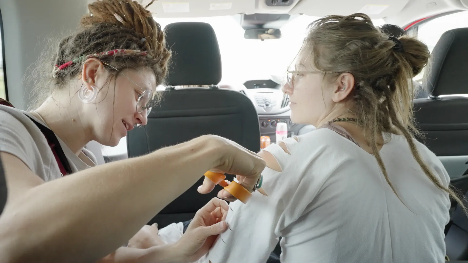 Two women with dreadlocks are sitting in the back seat of a car.