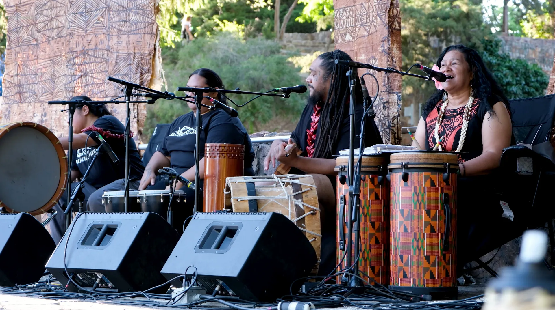 A group of people are playing drums and singing into microphones on a stage.