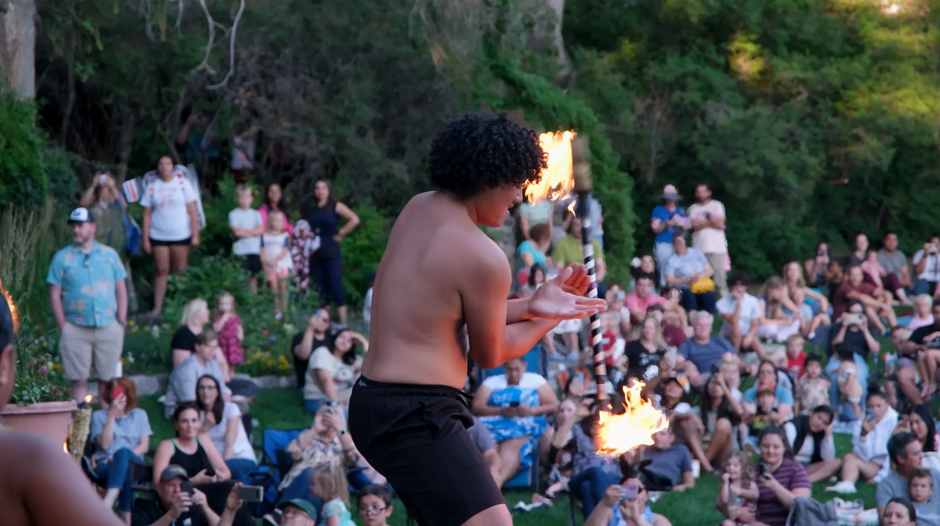A man without a shirt is juggling fire in front of a crowd of people.