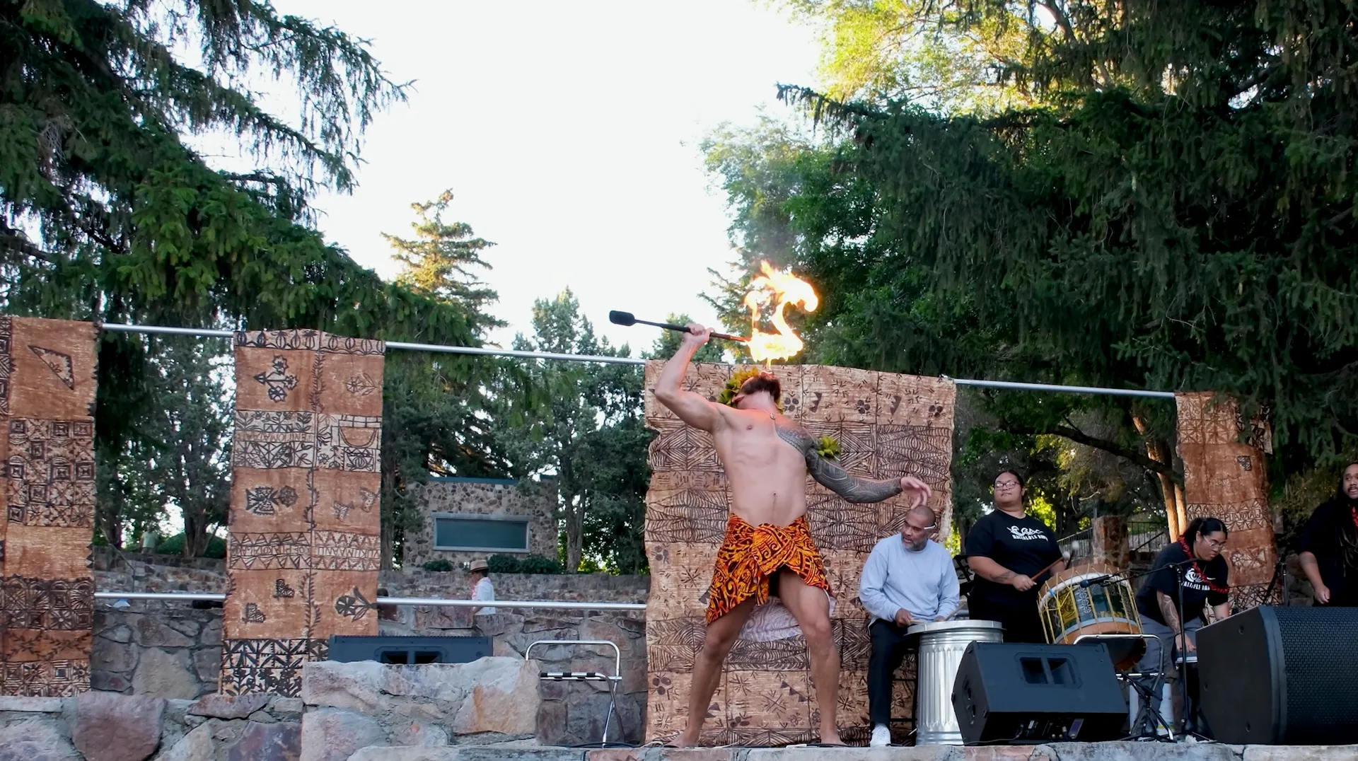 A man without a shirt is standing on a stage holding a fire torch.