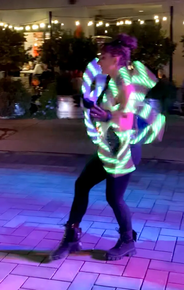 A woman in a neon outfit is dancing on a brick floor.
