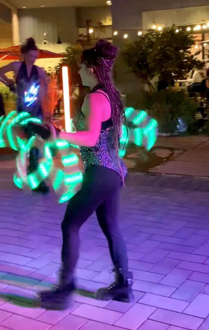 A woman is standing on a sidewalk holding glowing lightsabers.