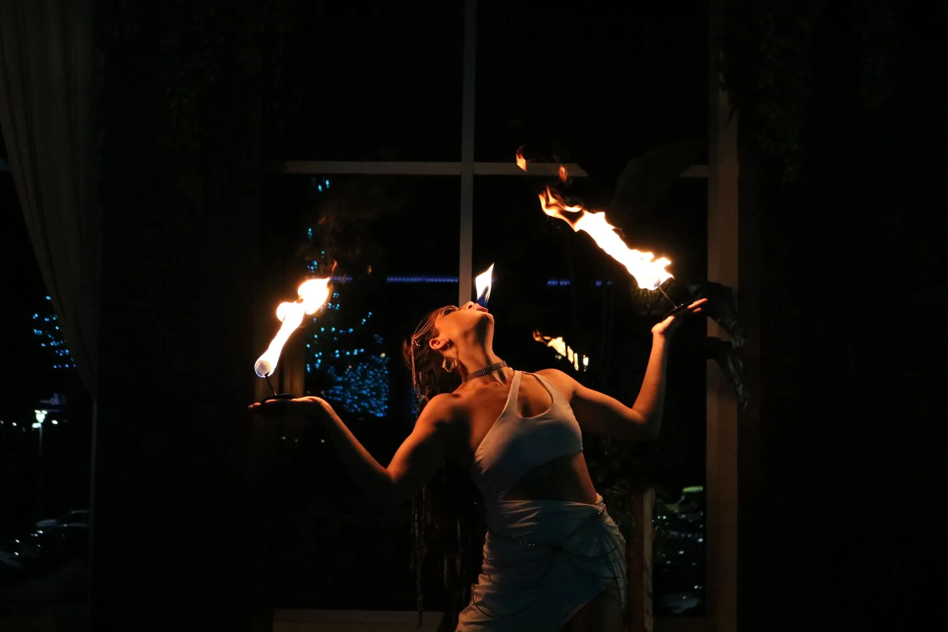 A woman is holding two fire torches in her hands in a dark room.
