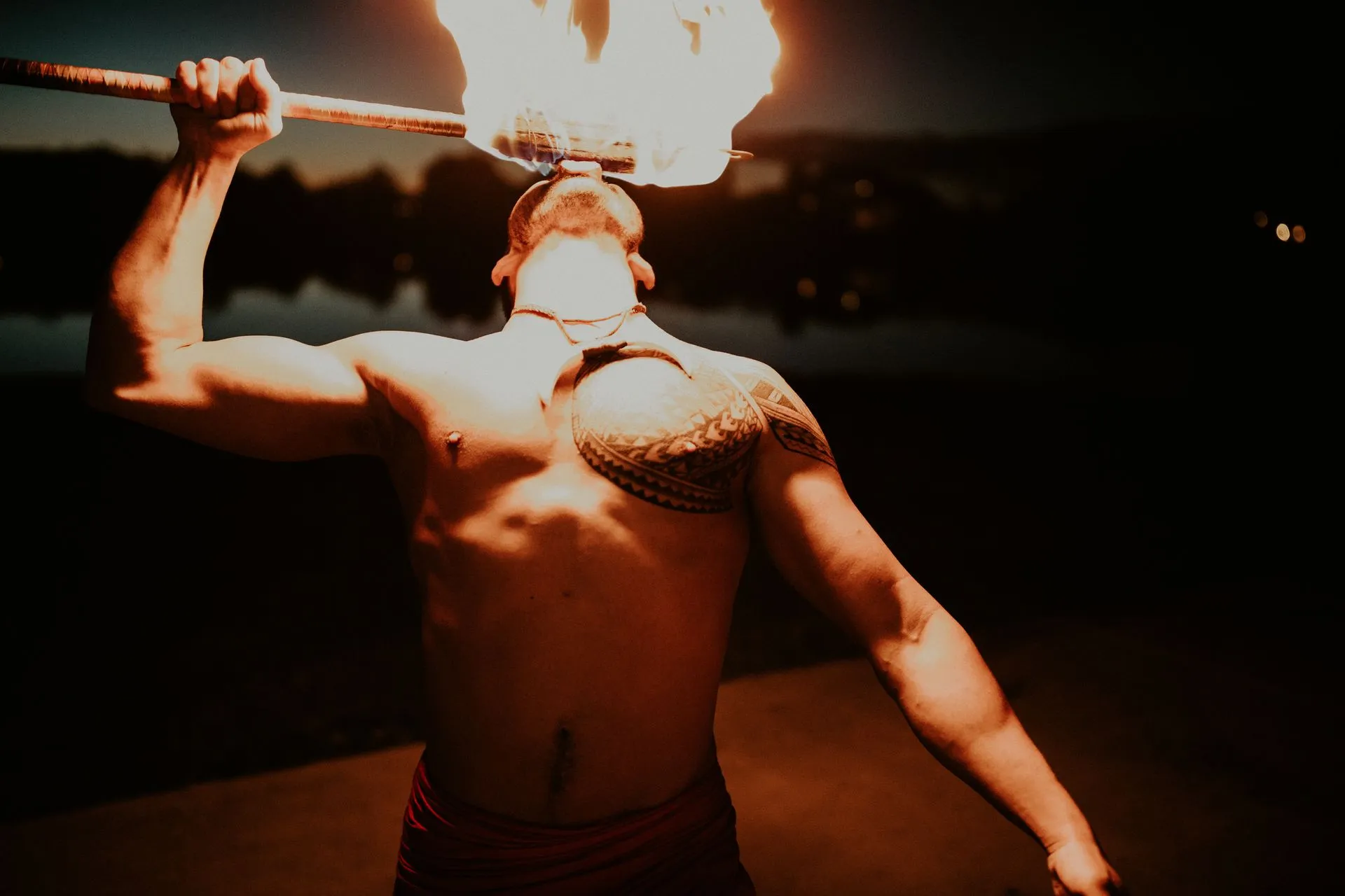 A shirtless man is holding a torch in front of his face.