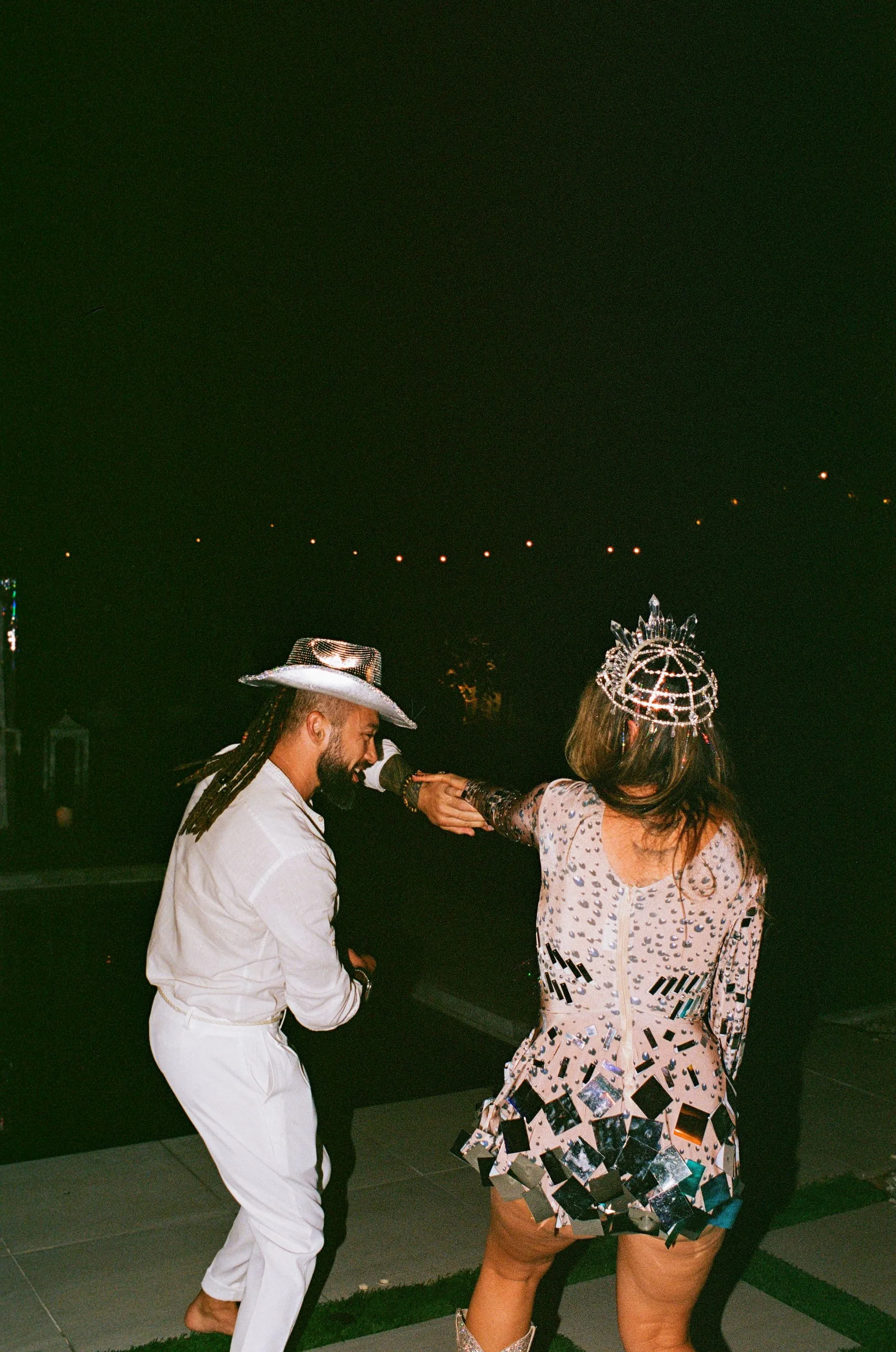 Man and person dance at night. They wear white and a bedazzled outfit with a crown.