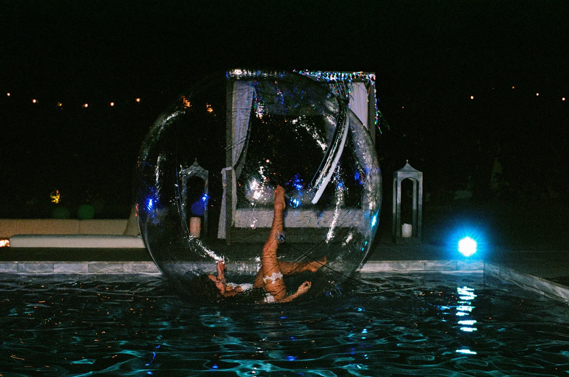 Synchronized swimmer performs inside a large glass bubble in a dark pool at night.