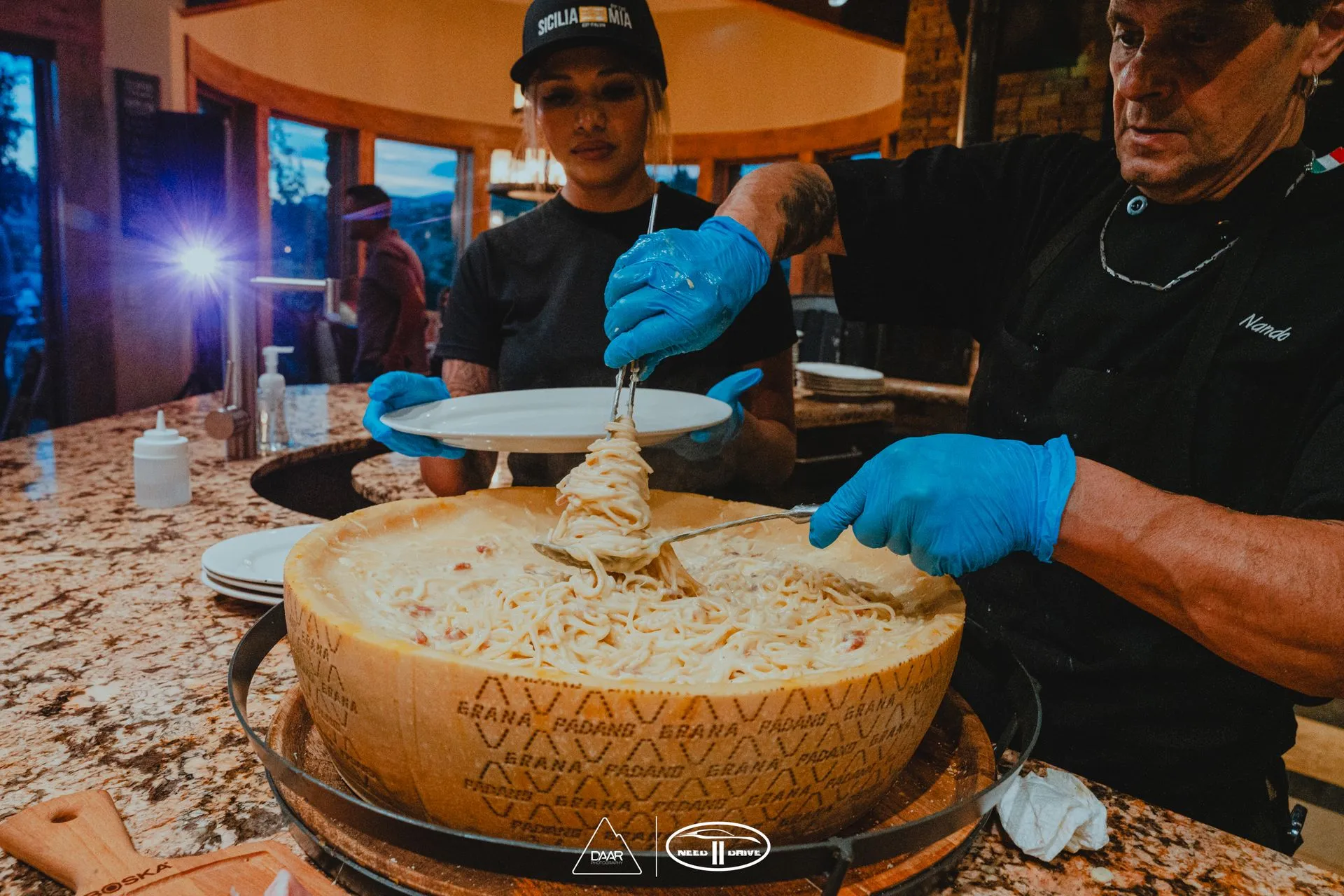 A man and a woman are cutting a large piece of cheese.