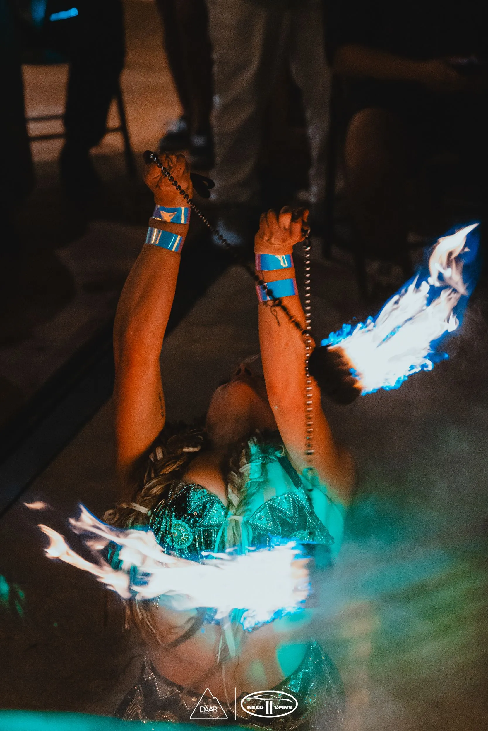 A woman in a belly dancer costume is holding a pair of fire sticks.