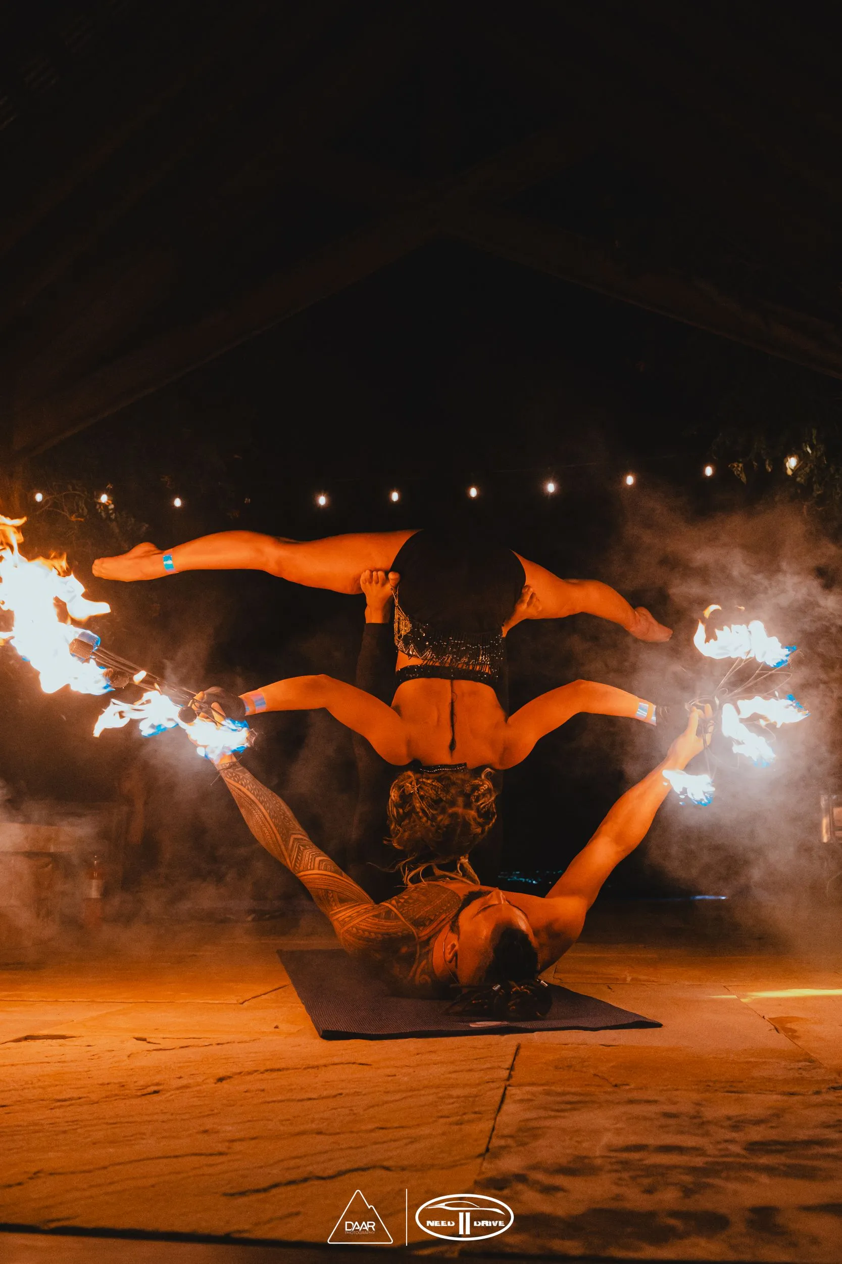 A man and a woman are doing a handstand with fire sticks.