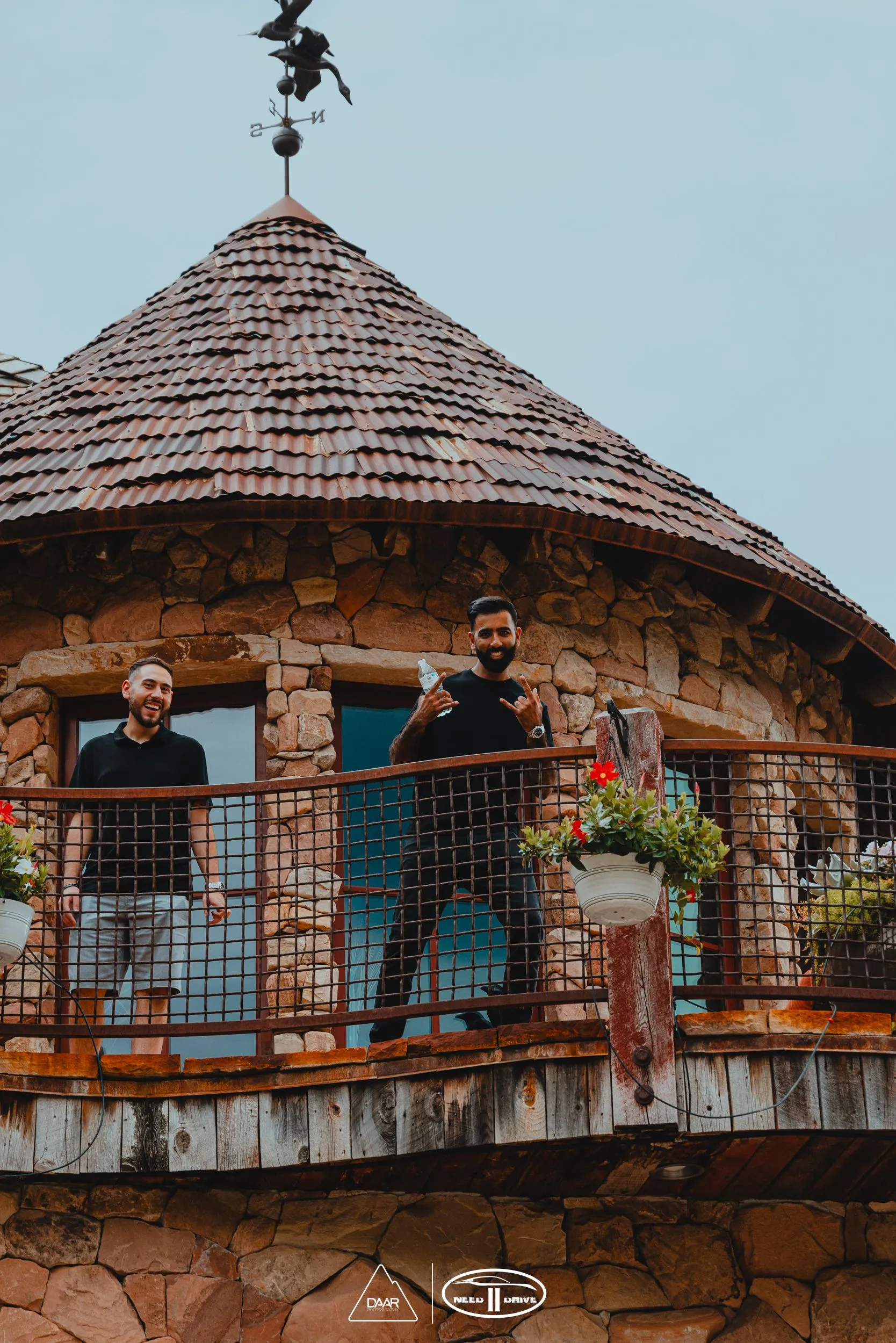 Two men are standing on a balcony of a stone building.