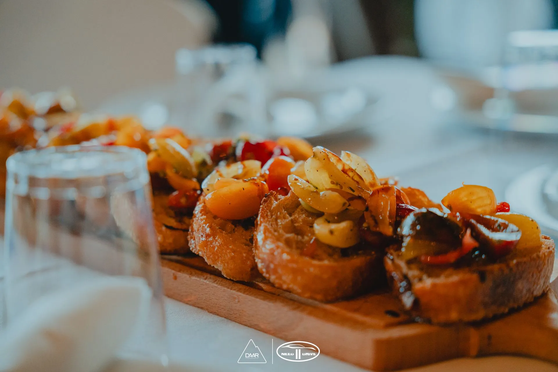 A wooden cutting board topped with bread and vegetables on a table.