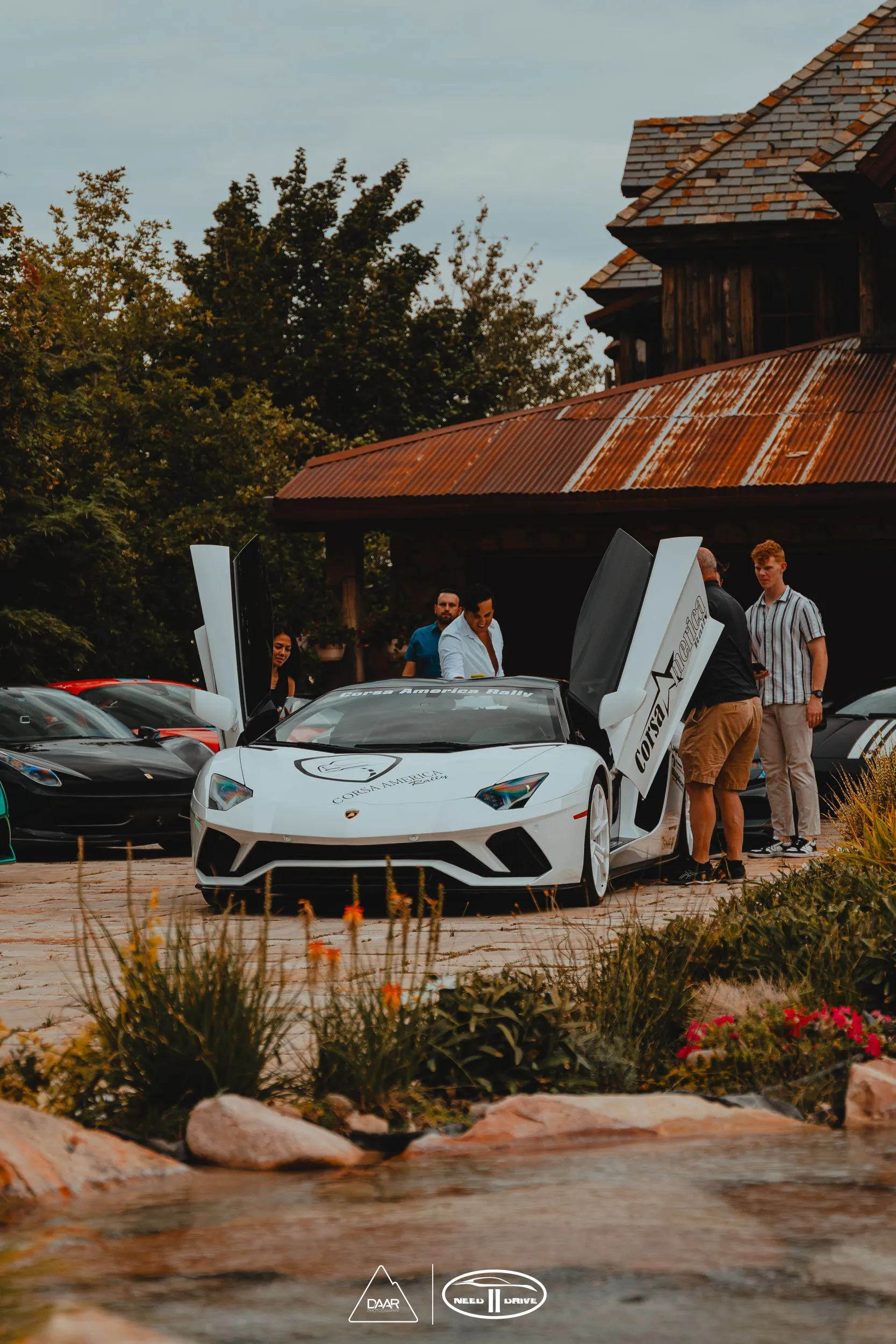 A white lamborghini aventador is parked in front of a house with its doors open.