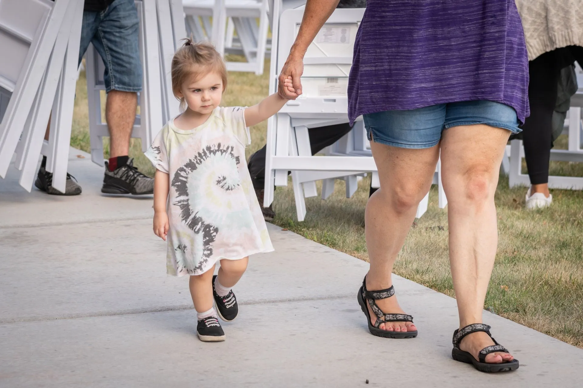 A little girl is holding a woman 's hand while walking down a sidewalk.