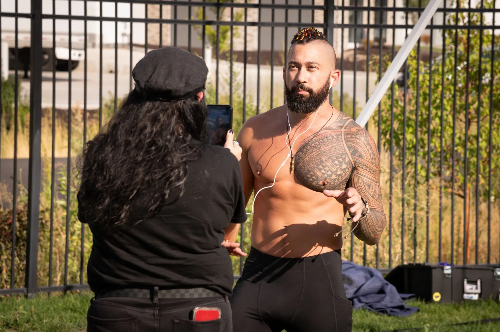 A woman is taking a picture of a shirtless man.