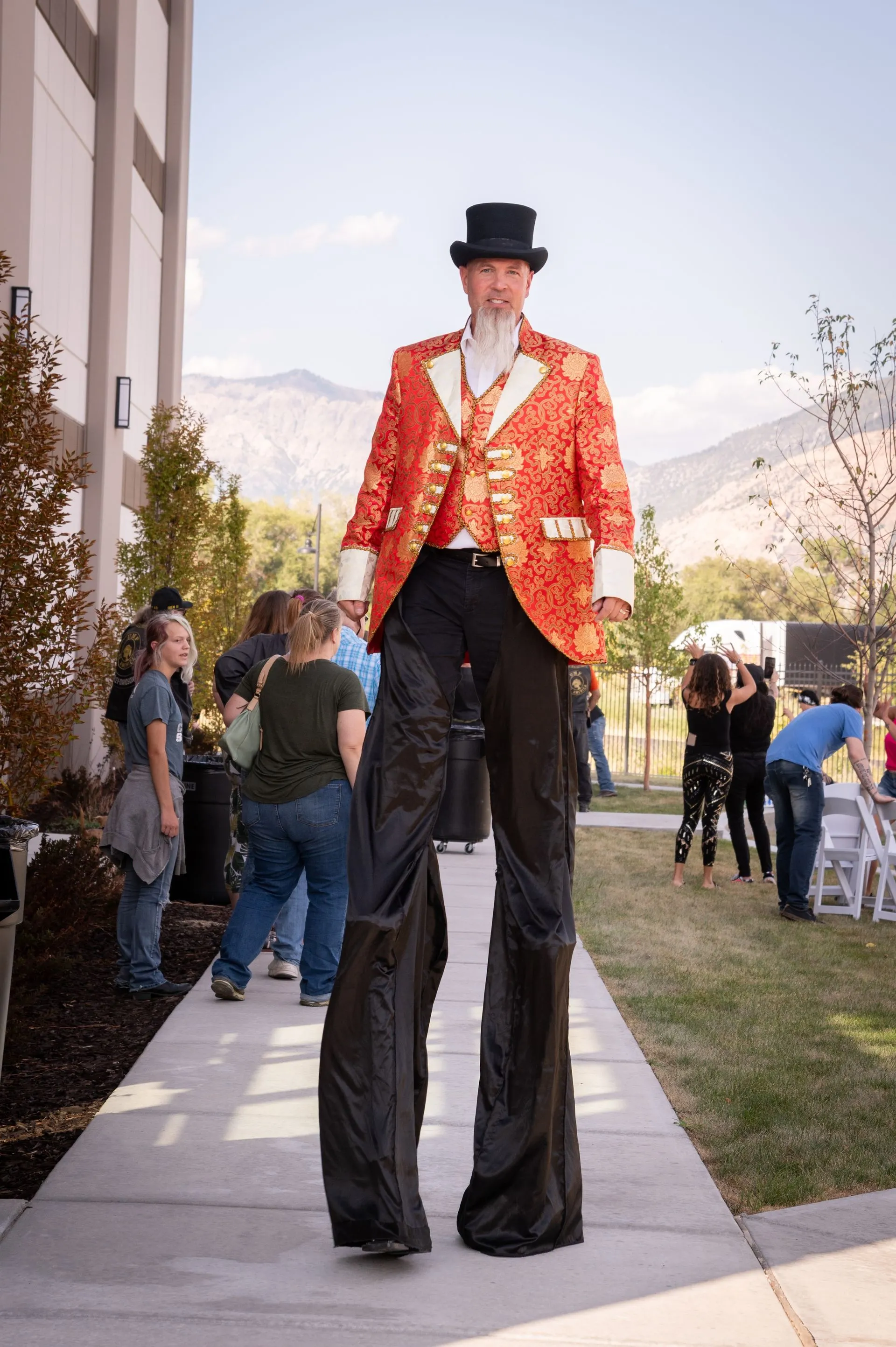A man wearing a top hat and stilts is walking down a sidewalk.