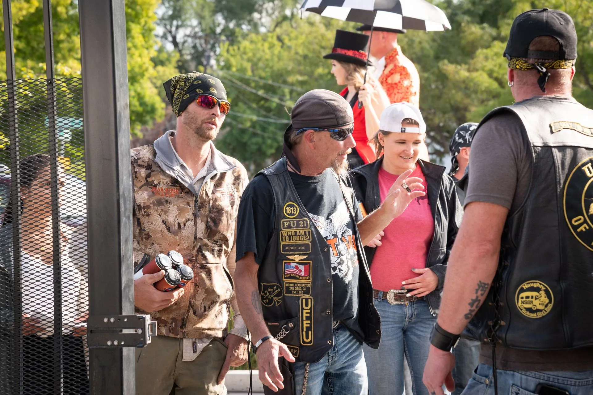 A group of people are standing in front of a fence talking to each other.