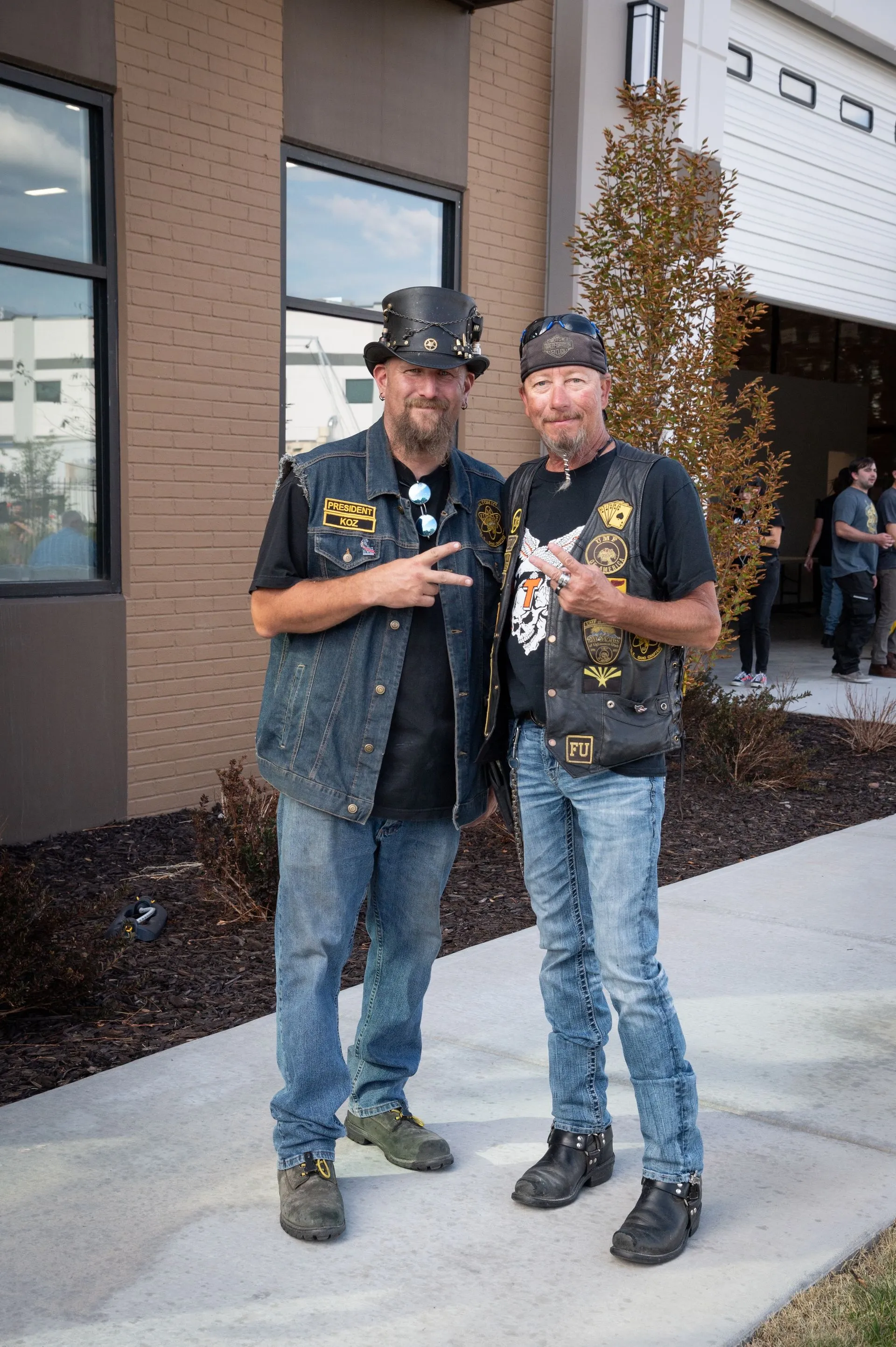 Two men are standing next to each other on a sidewalk in front of a building.