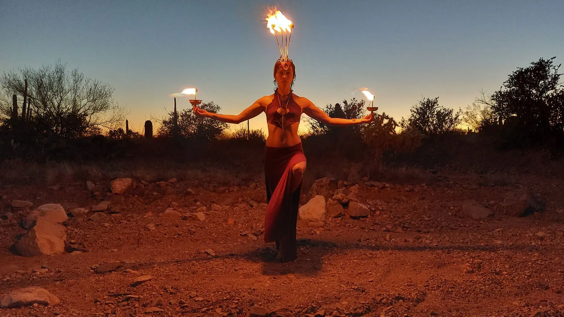 A woman is holding two fire torches in the desert