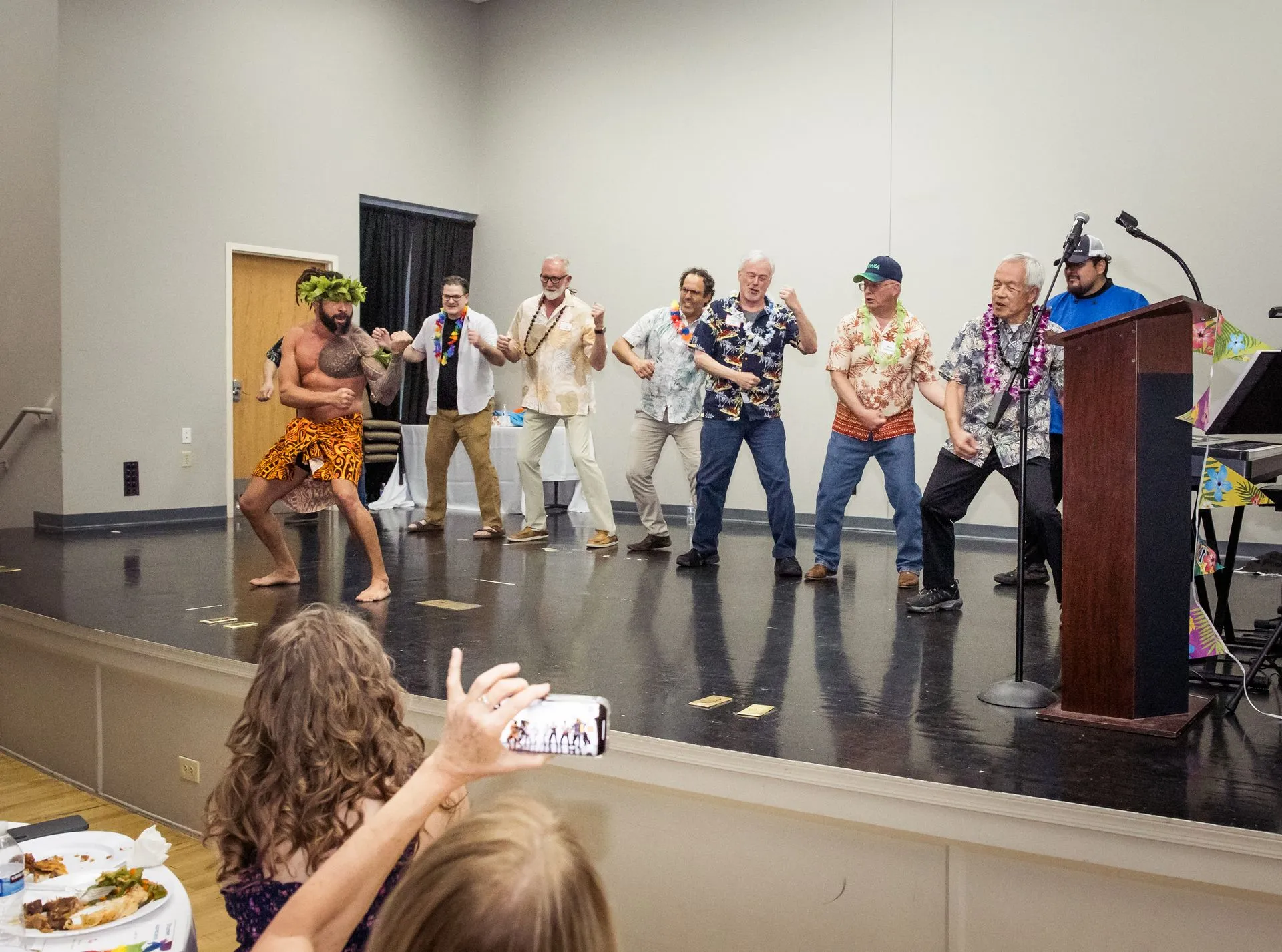 A girl is taking a picture of a group of people dancing on a stage.