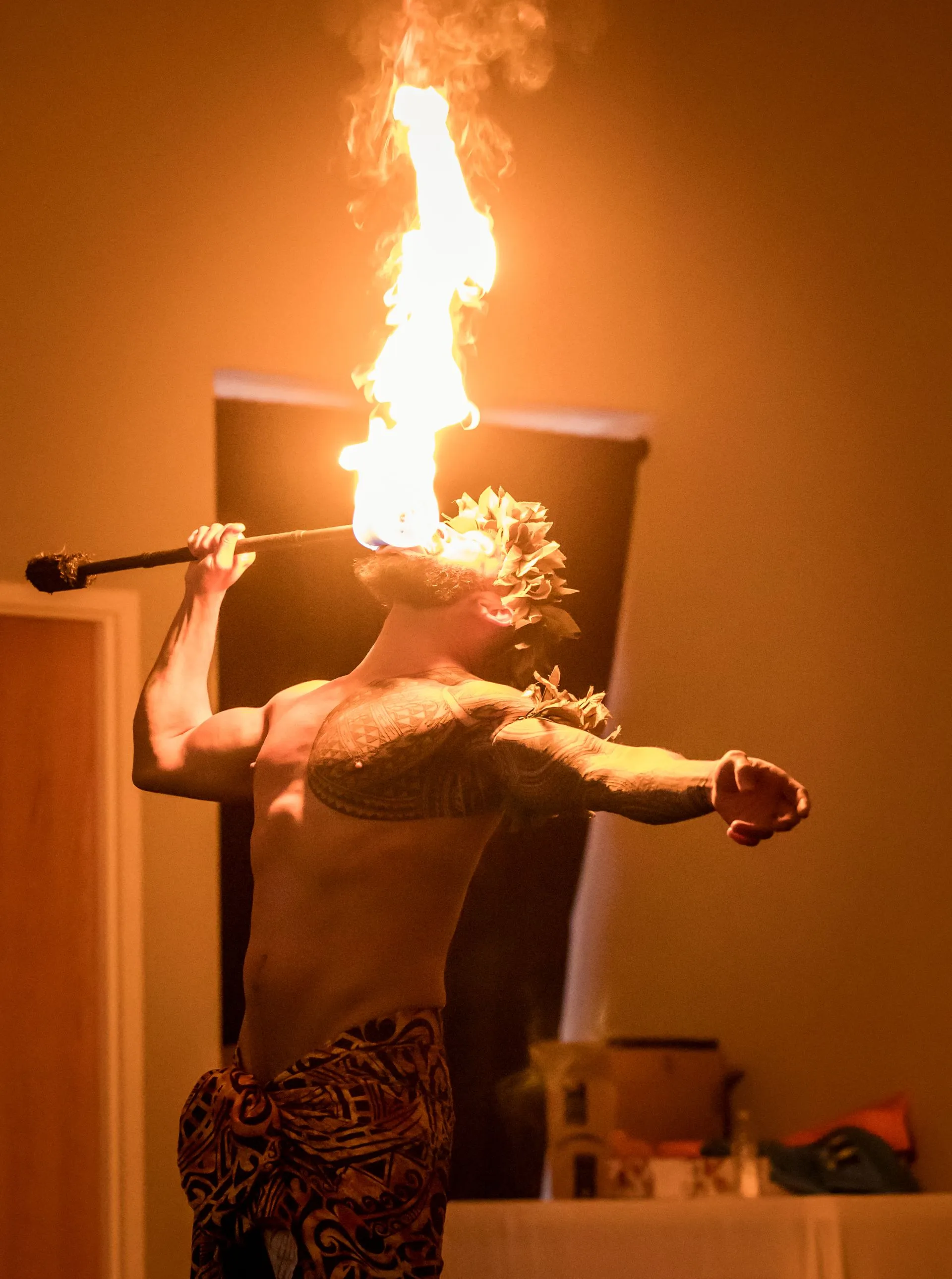 A shirtless man is holding a stick with flames coming out of it 's mouth.