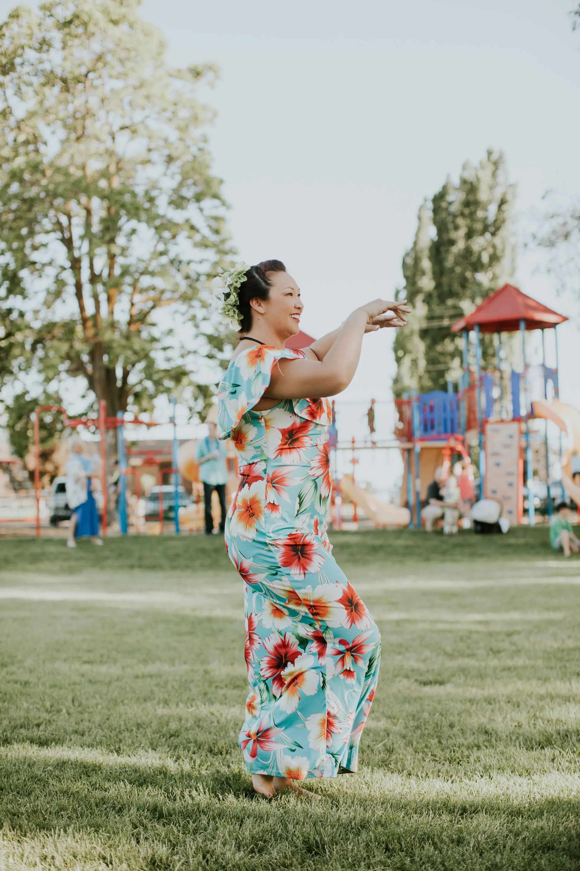 A woman in a floral dress is dancing in a park.