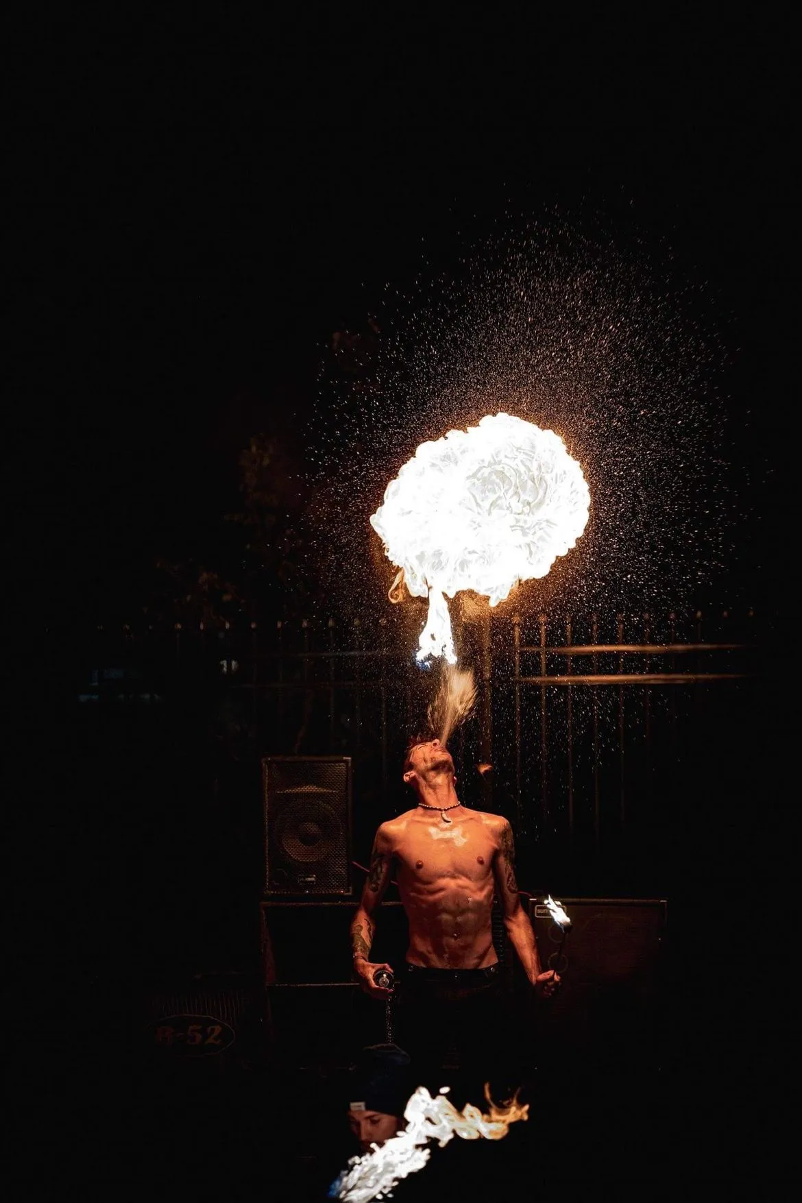 A man is blowing fire from his mouth in the dark.