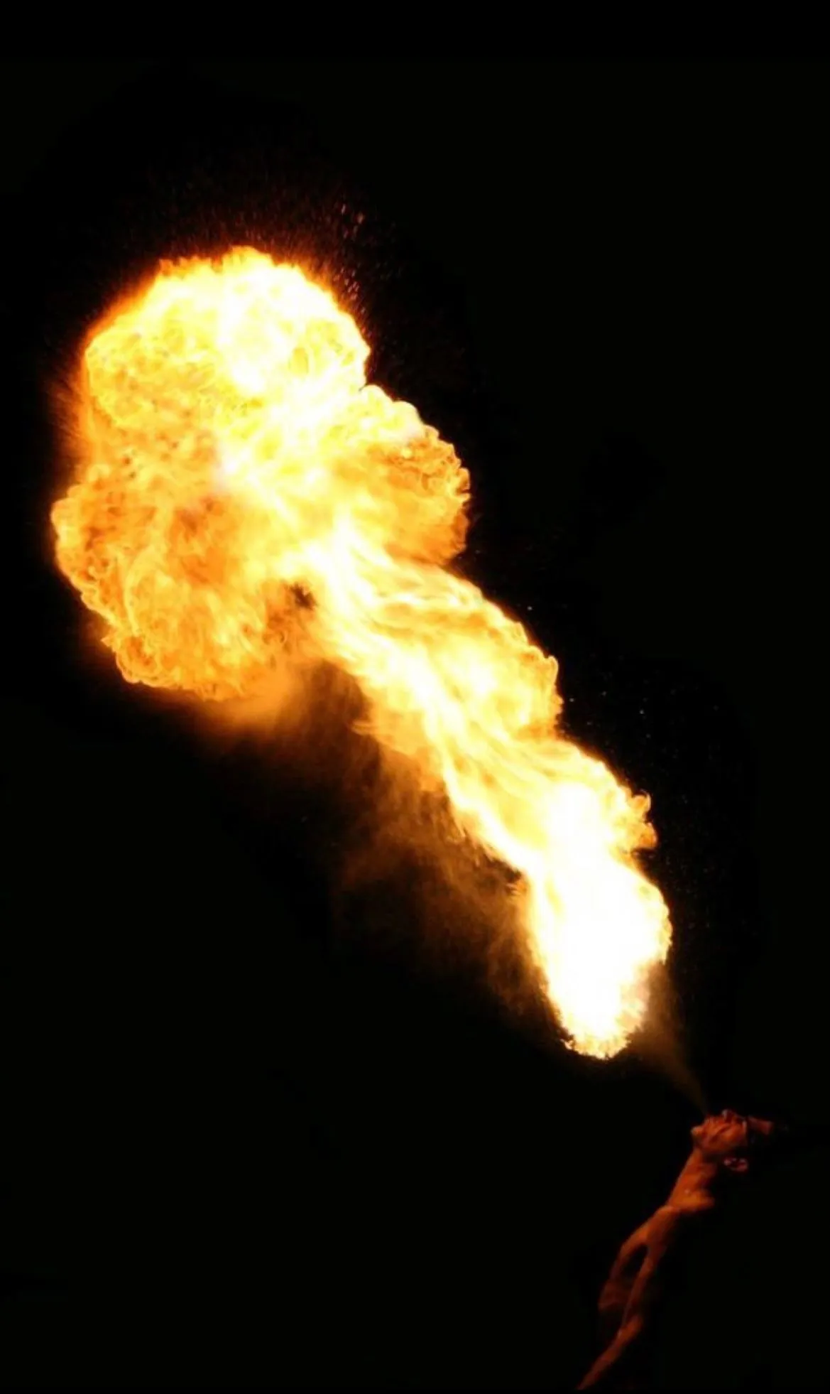 A flame is coming out of a person 's mouth in the dark.