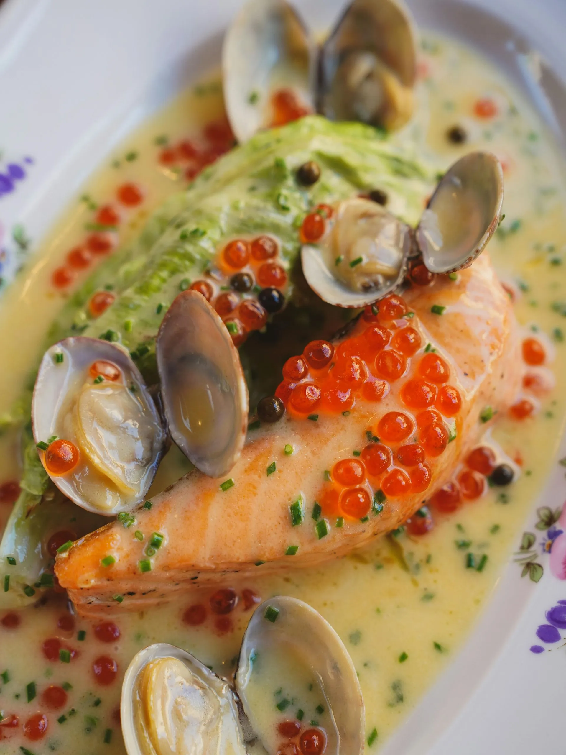 Salmon dish with clams, caviar, and sauce on a decorative plate.
