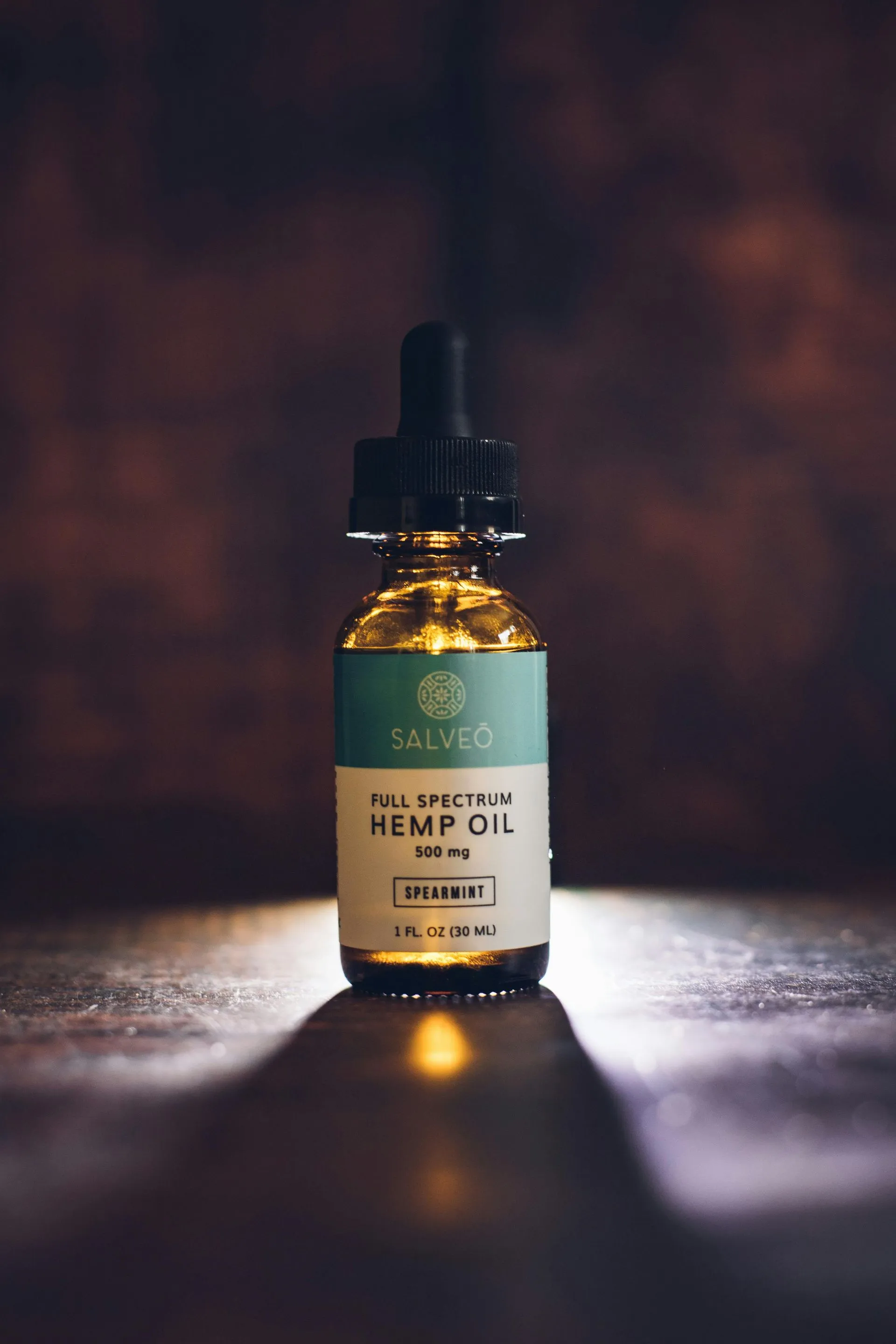 Amber bottle of Salved full-spectrum hemp oil with dropper on a dark, textured surface.