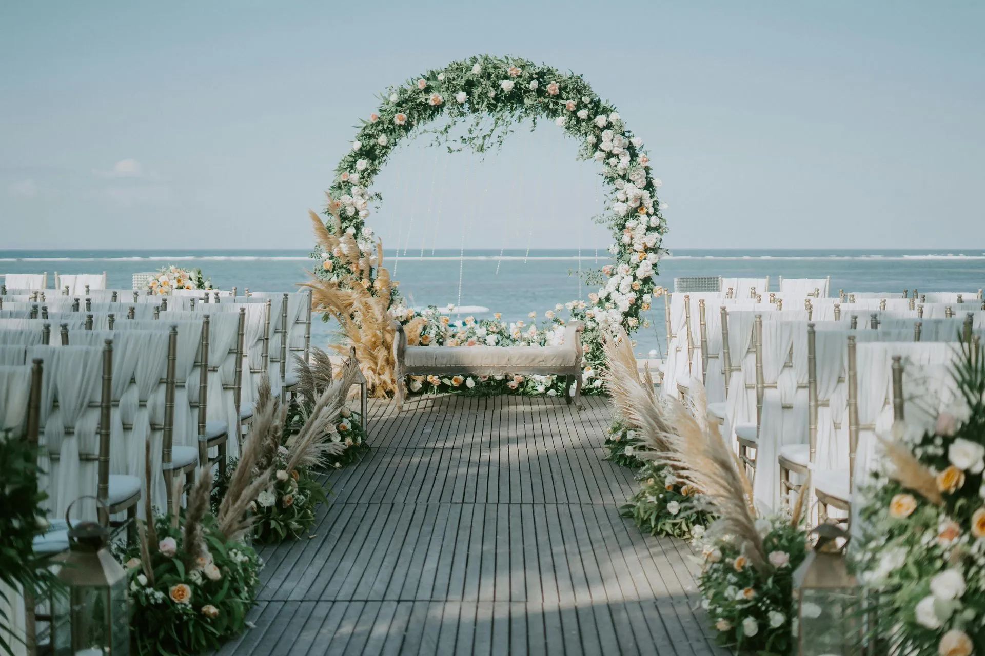 Wedding ceremony setup on a boardwalk overlooking the ocean, with a floral arch and seating.