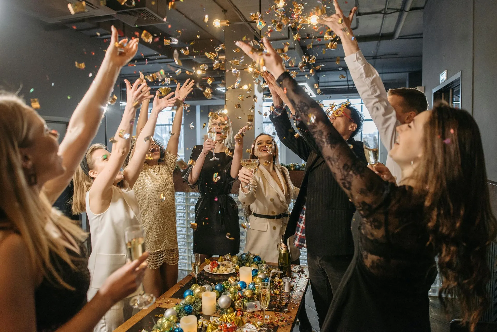 People at a party toss confetti. They are gathered around a table with decorations, celebrating.