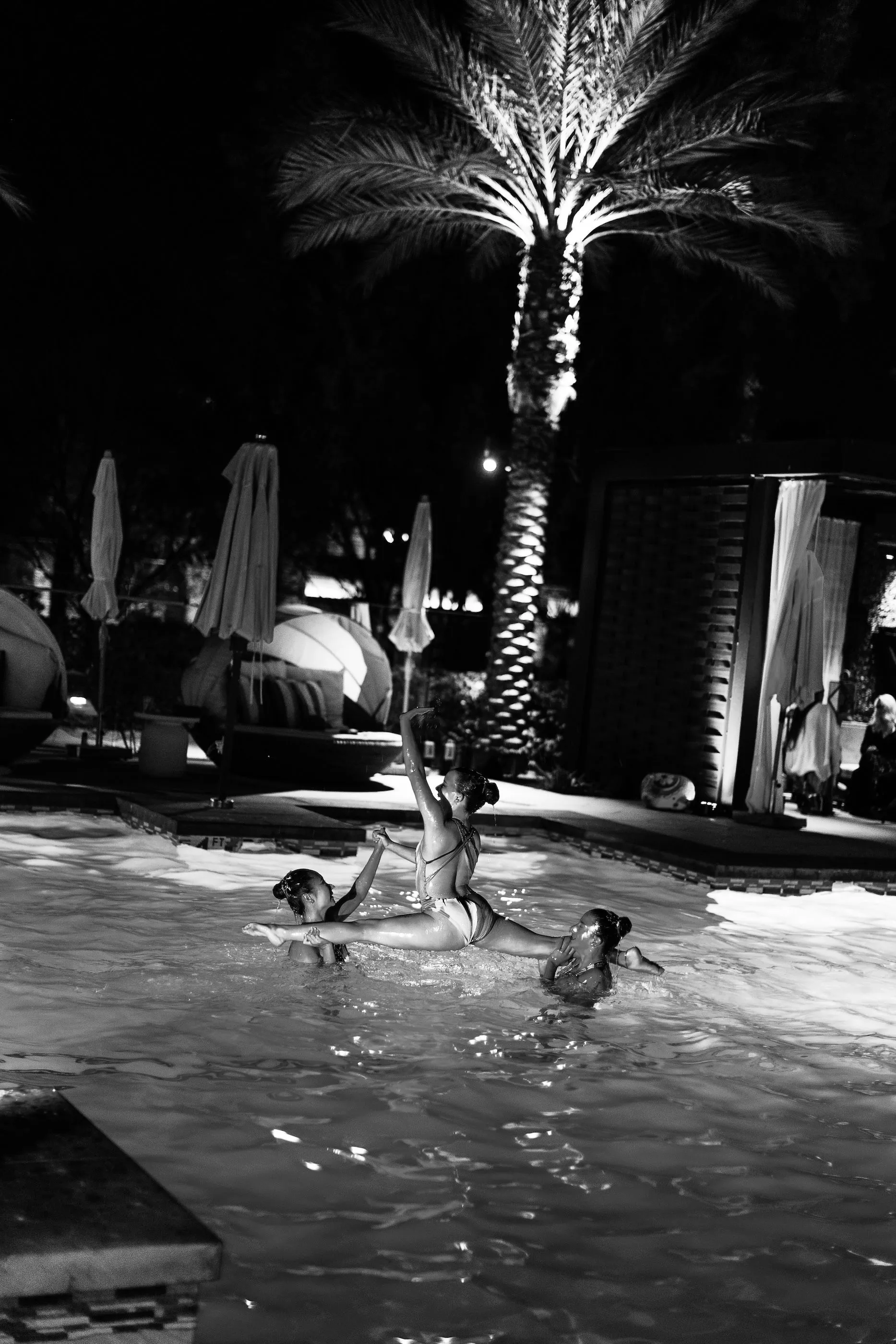 A group of people are swimming in a pool at night.
