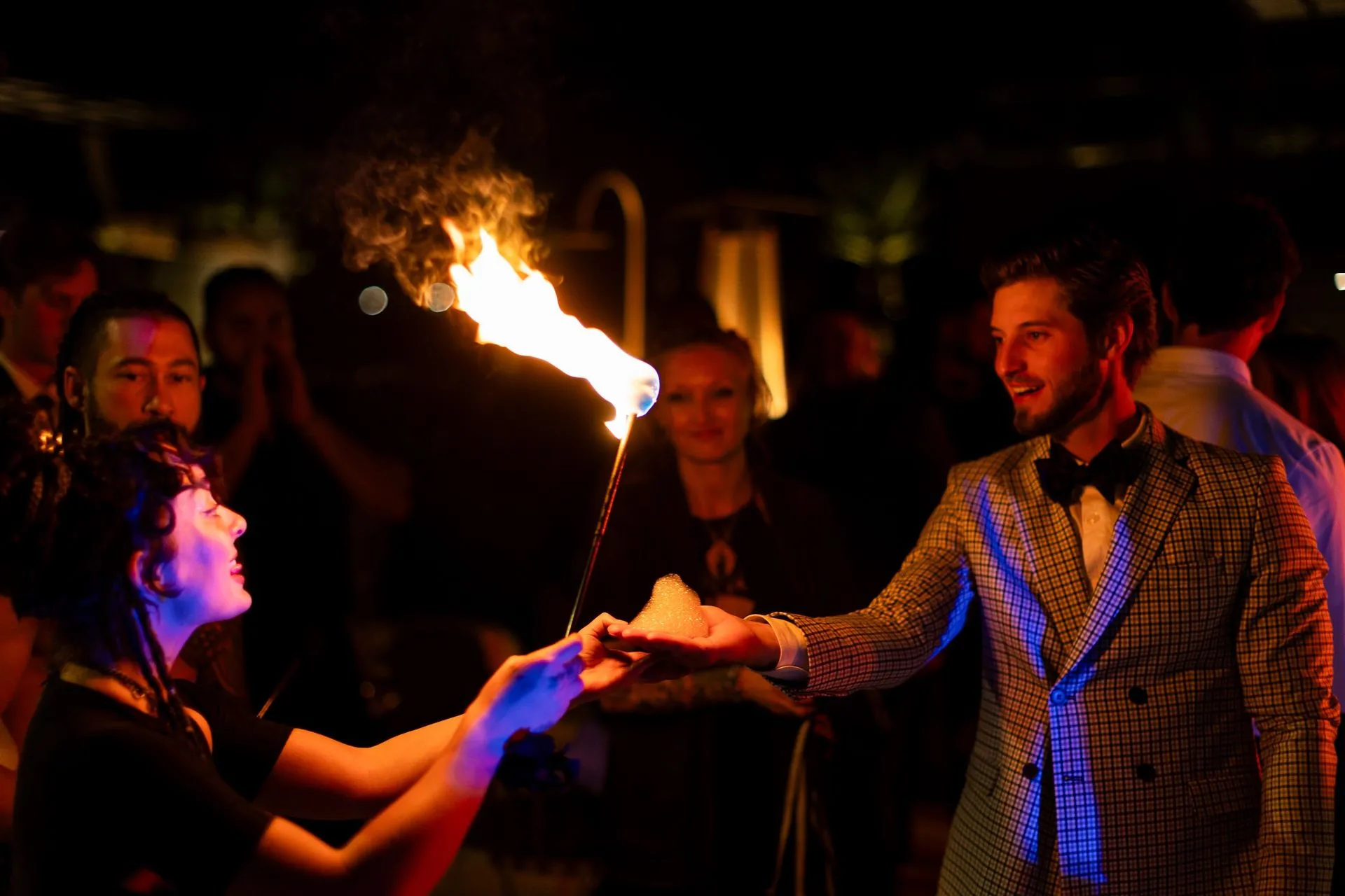 A man in a suit is holding a fire torch in front of a woman.