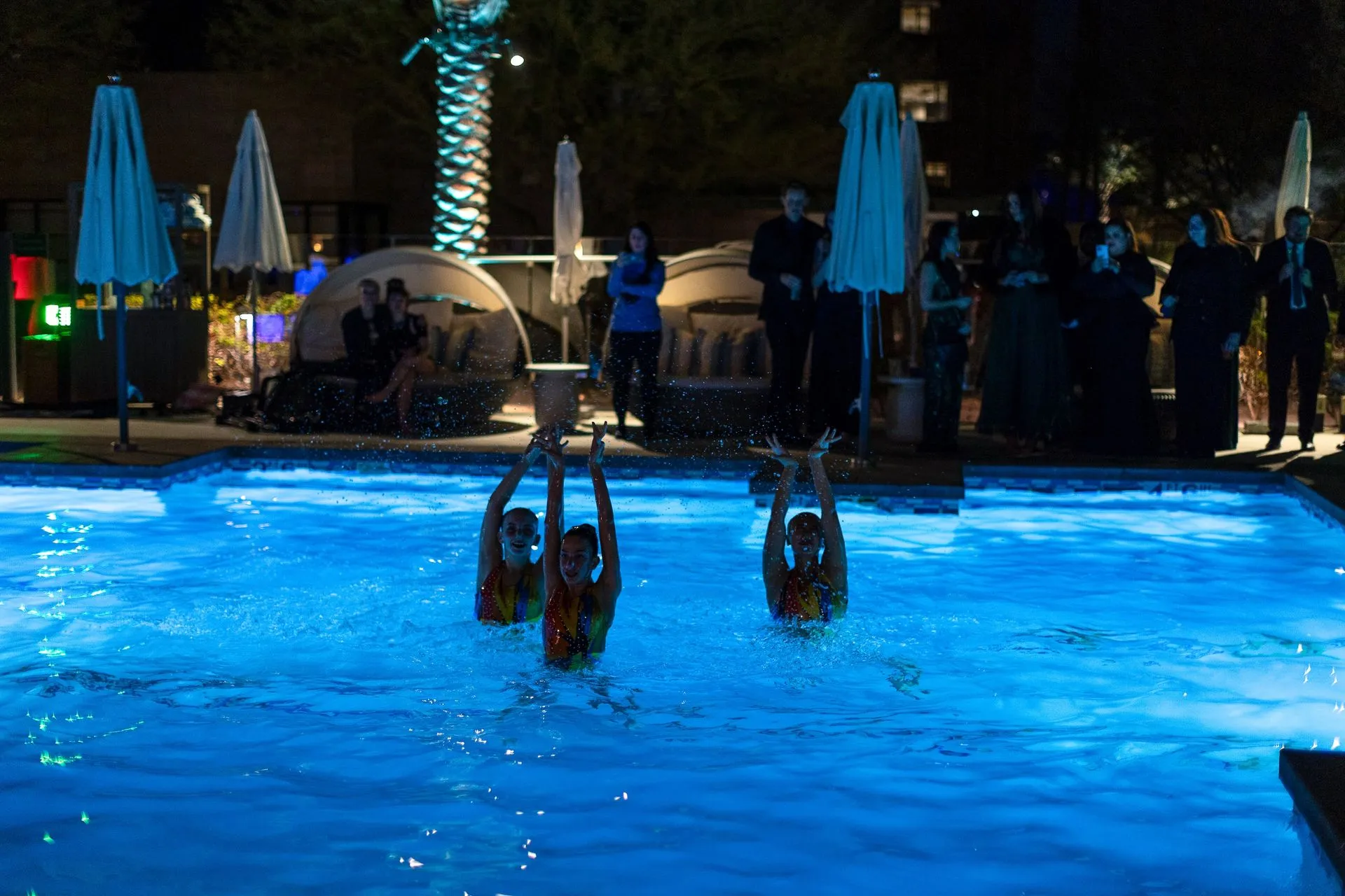 A group of people are standing around a swimming pool at night.