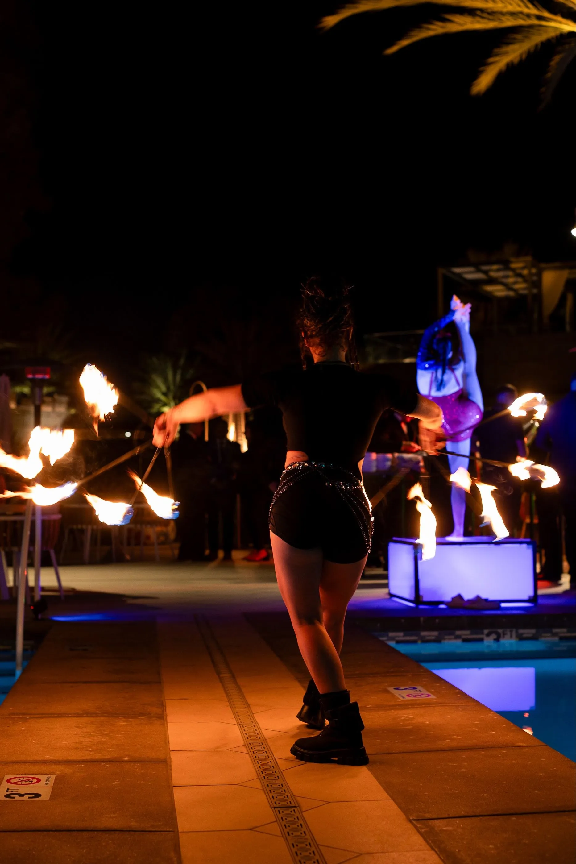 A woman is standing next to a pool holding a stick of fire.