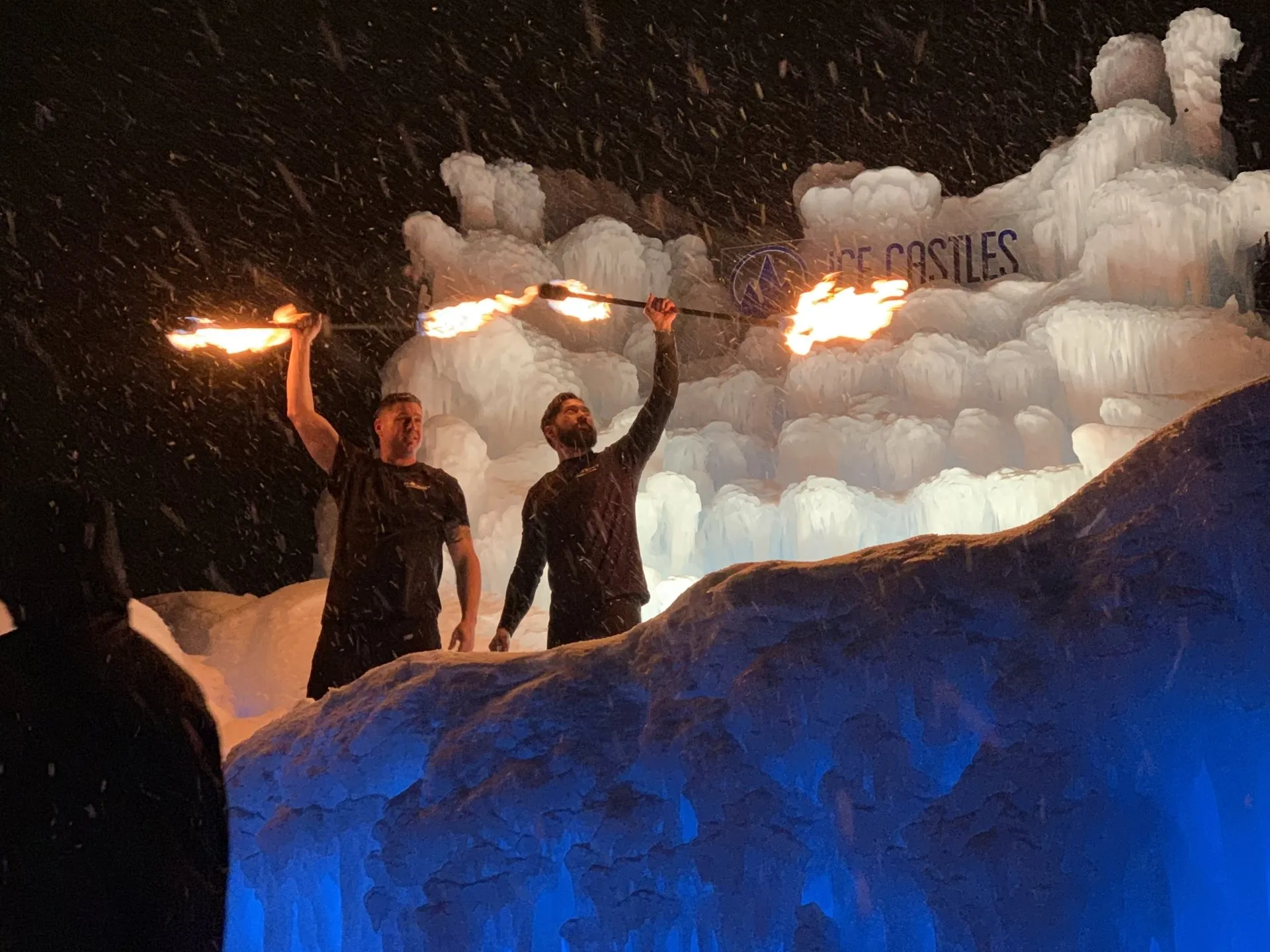 Two men are holding fire torches in front of a large ice sculpture.