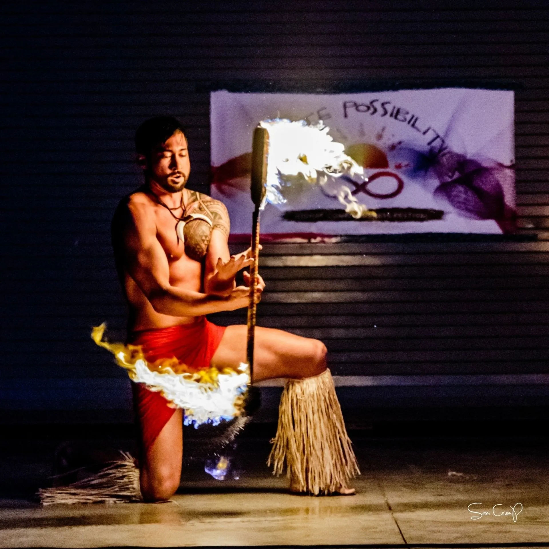 A man is kneeling down holding a fire stick in front of a sign that says possibility