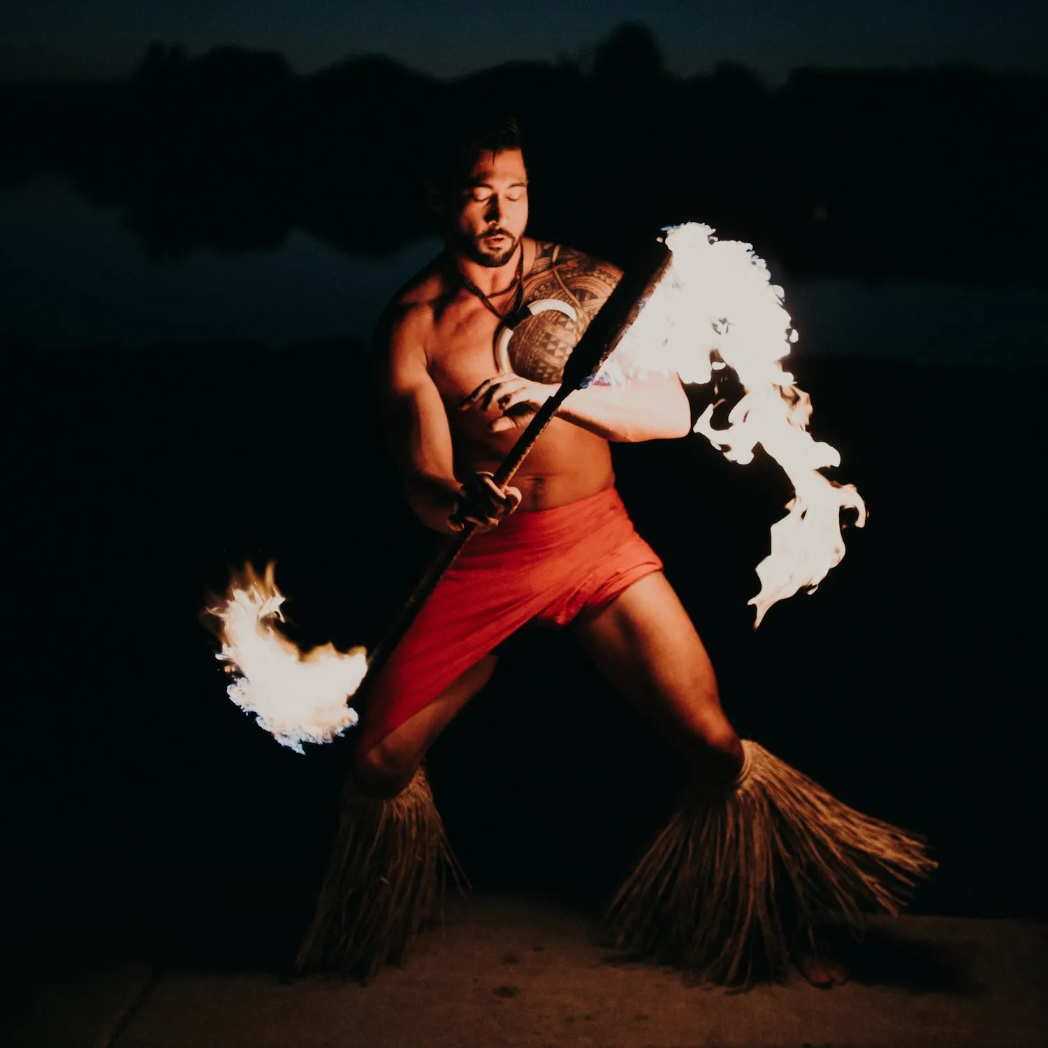 A man in a red skirt is holding a torch with flames coming out of it
